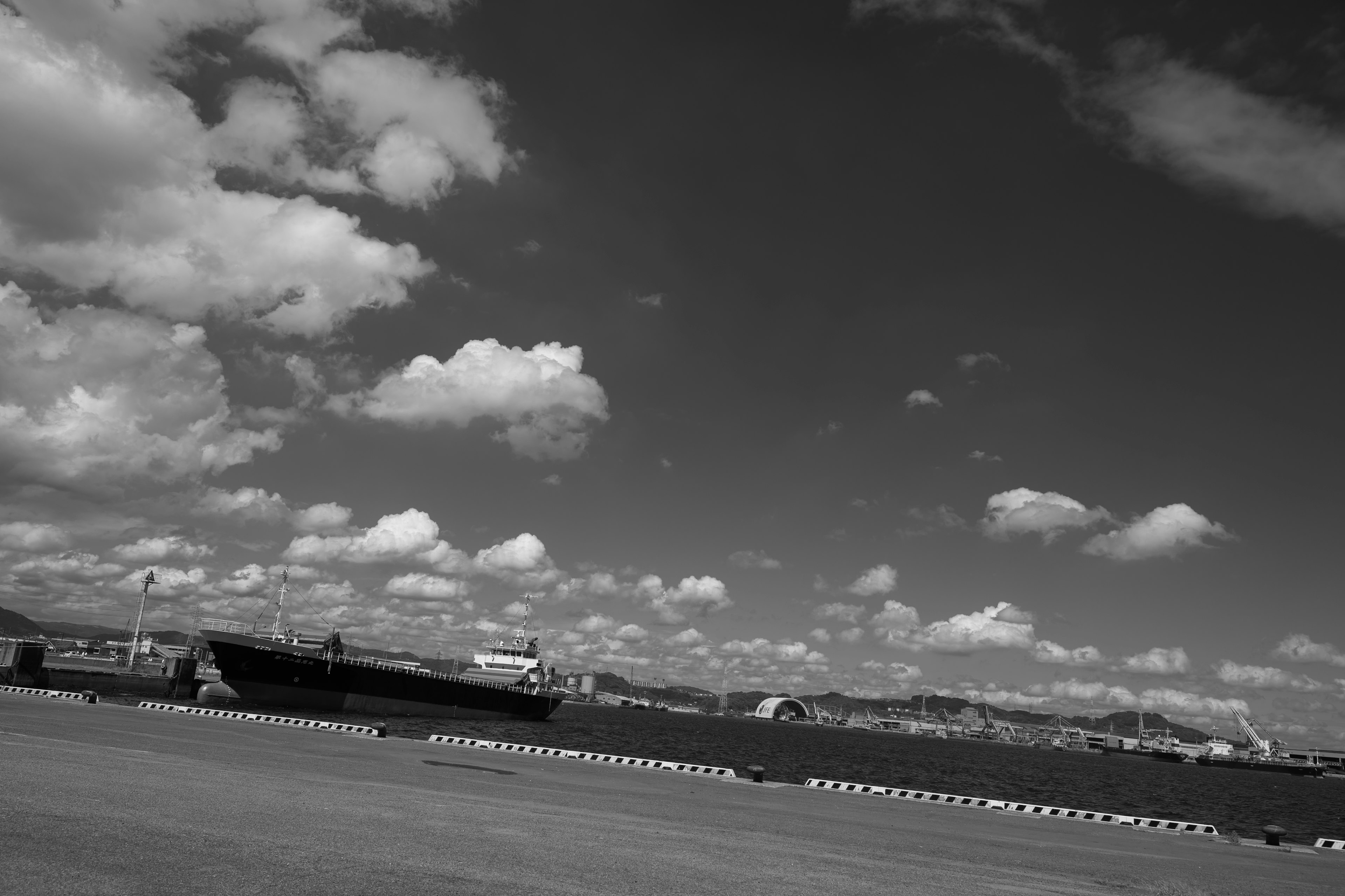 A black and white landscape of a harbor with clouds in the sky