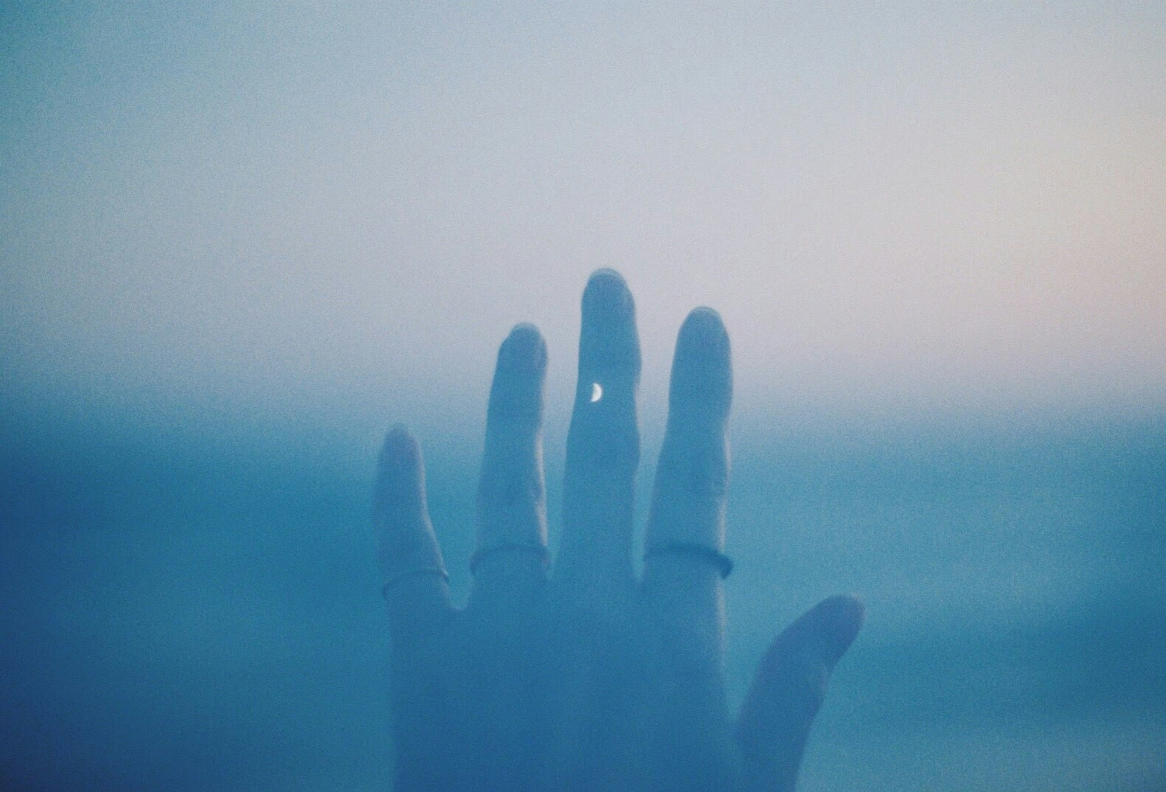 Silhouette of a hand reaching towards a blue ocean with rings on fingers