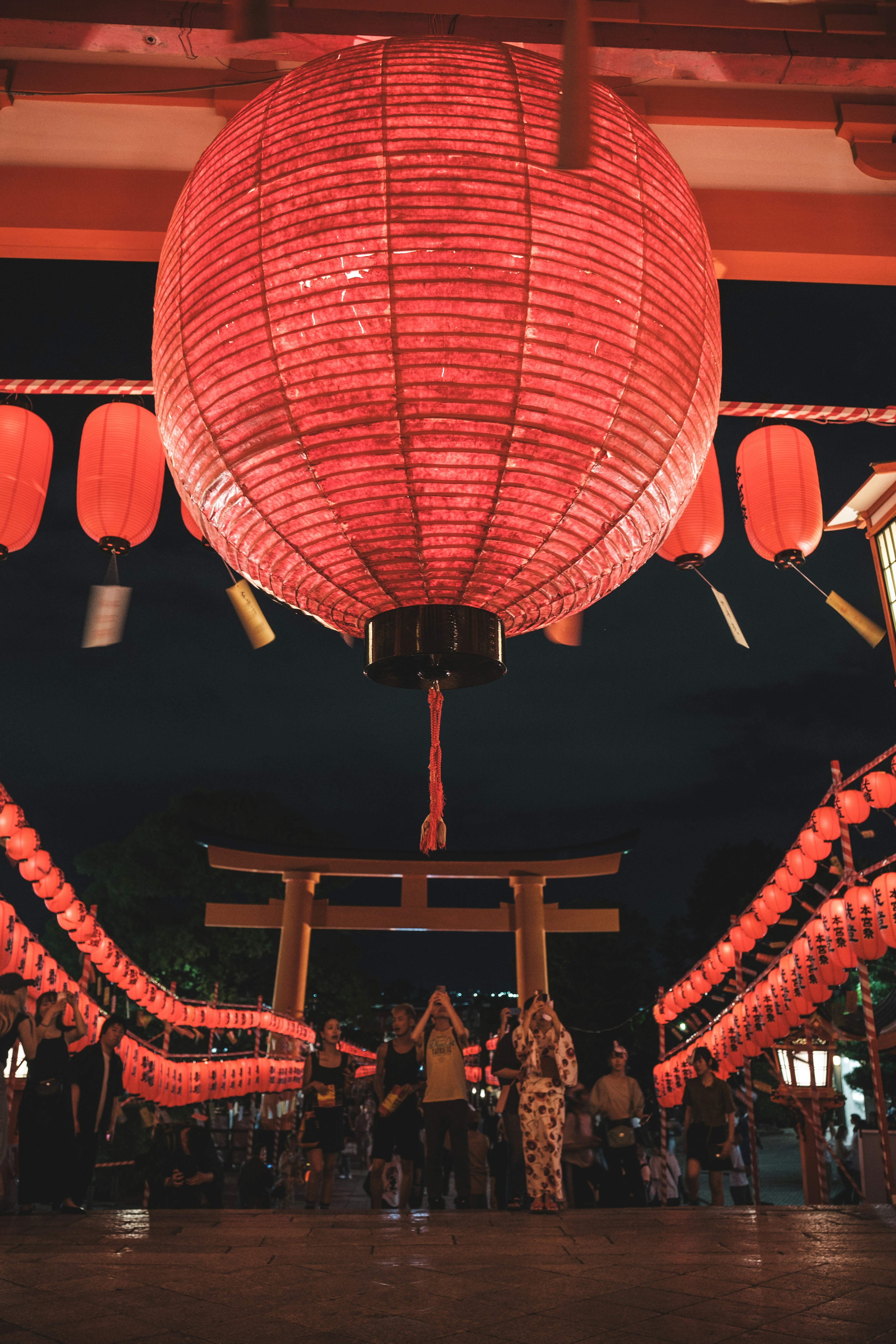 赤い提灯が吊るされた夜の祭りの雰囲気を持つ場所で人々が集まっている