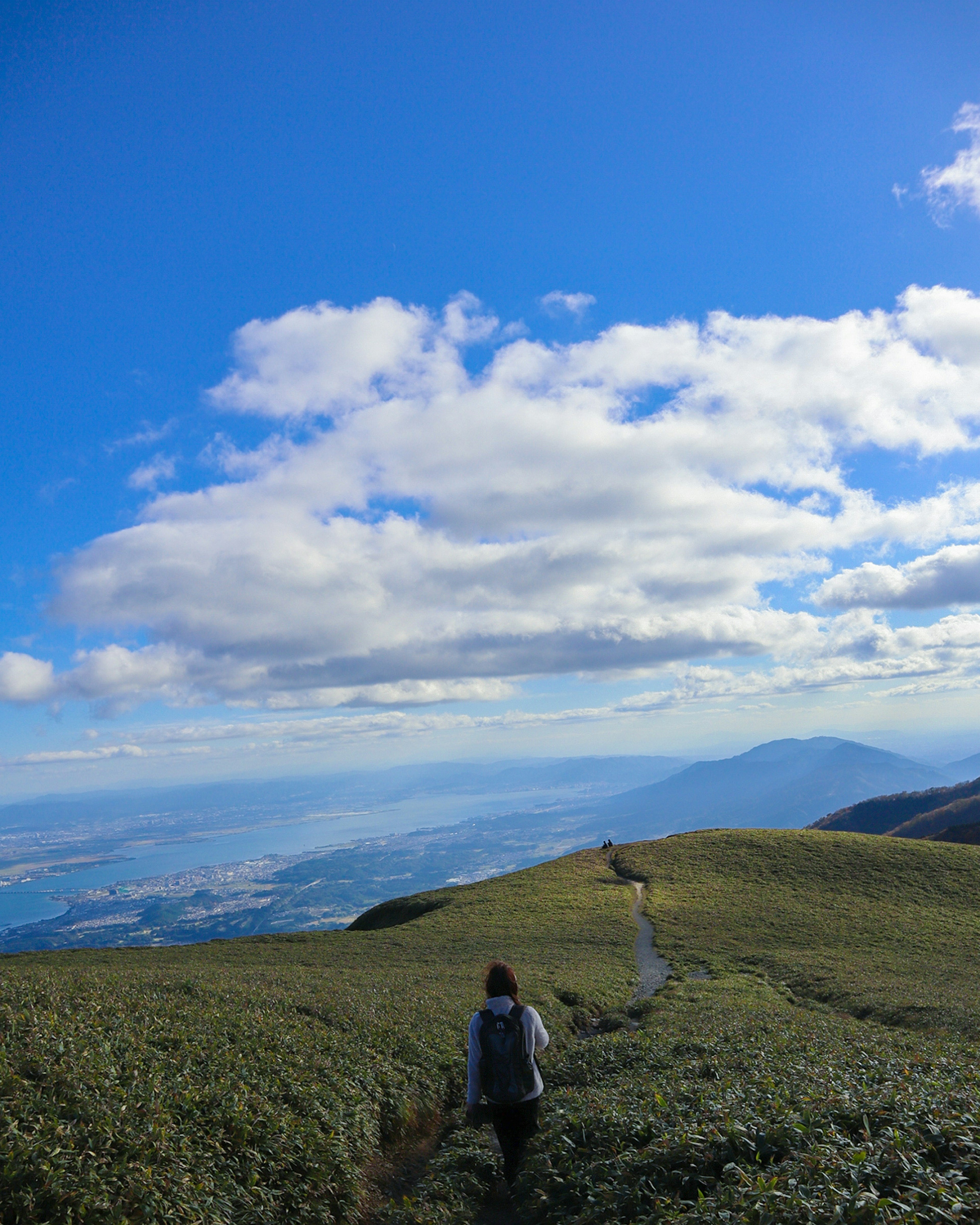 Un randonneur marchant à travers un paysage verdoyant sous un ciel bleu avec des nuages