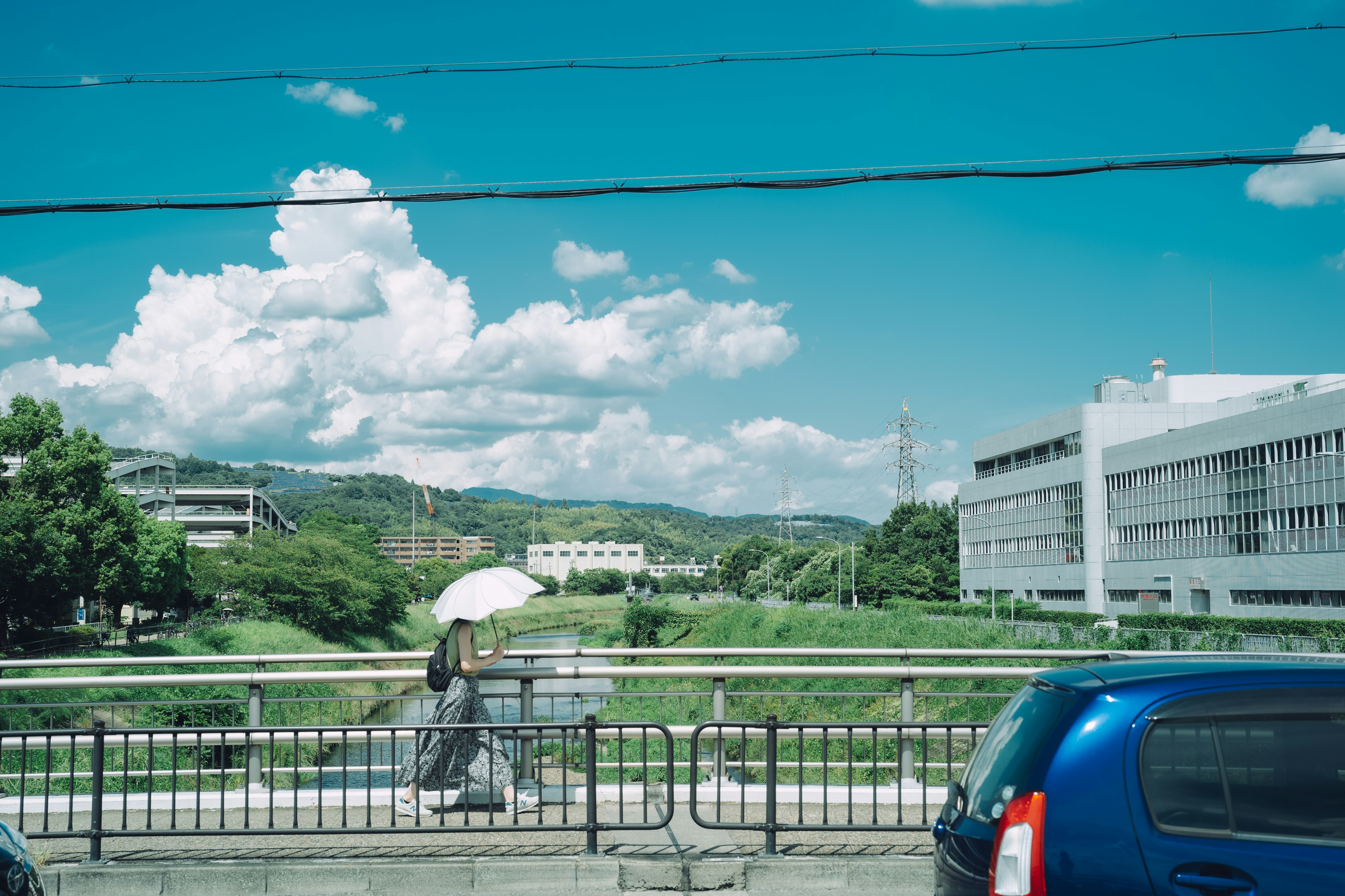 A woman walking with an umbrella under a blue sky and white clouds by a river