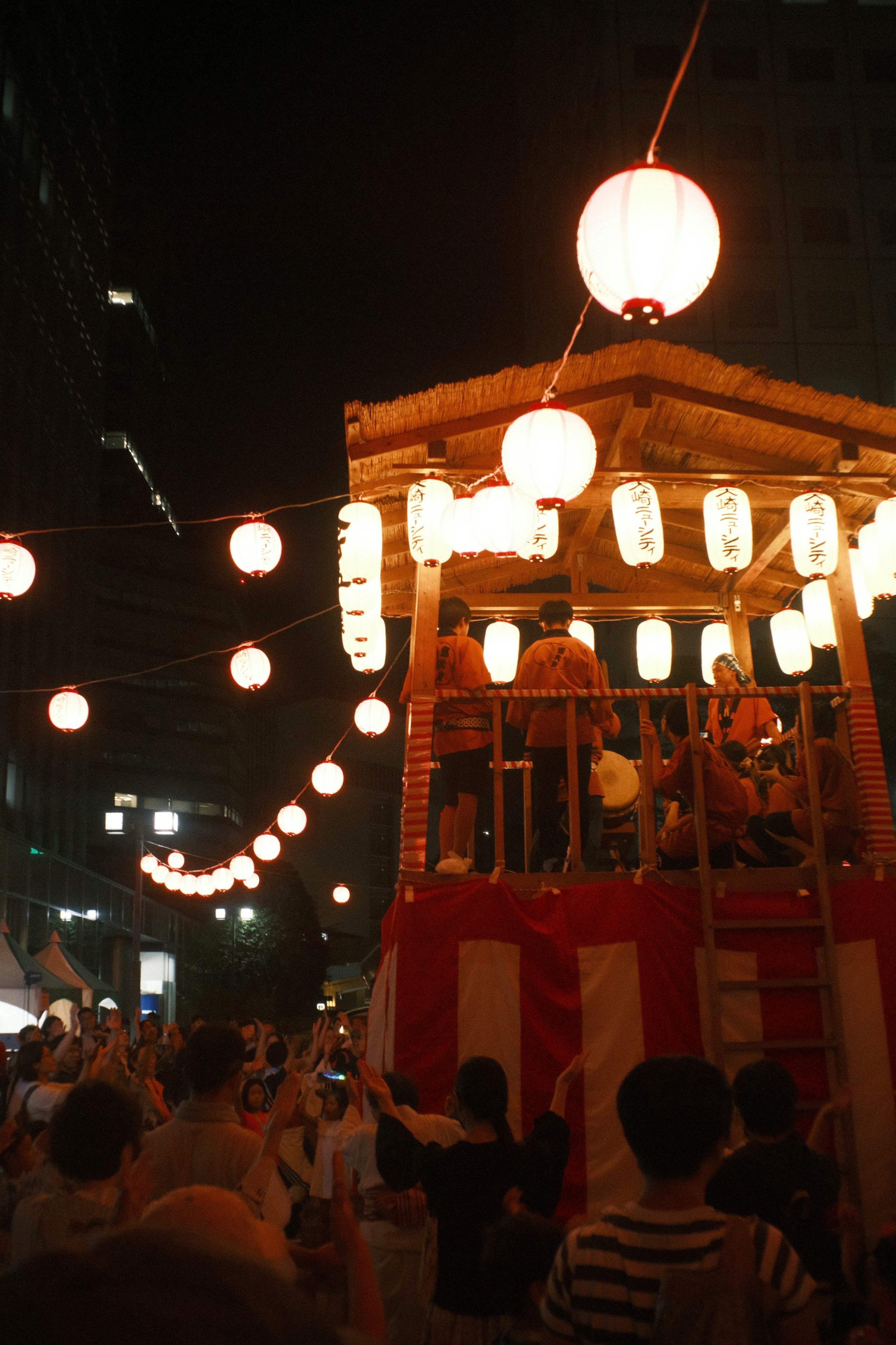 Night festival scene featuring illuminated lanterns and a festival float