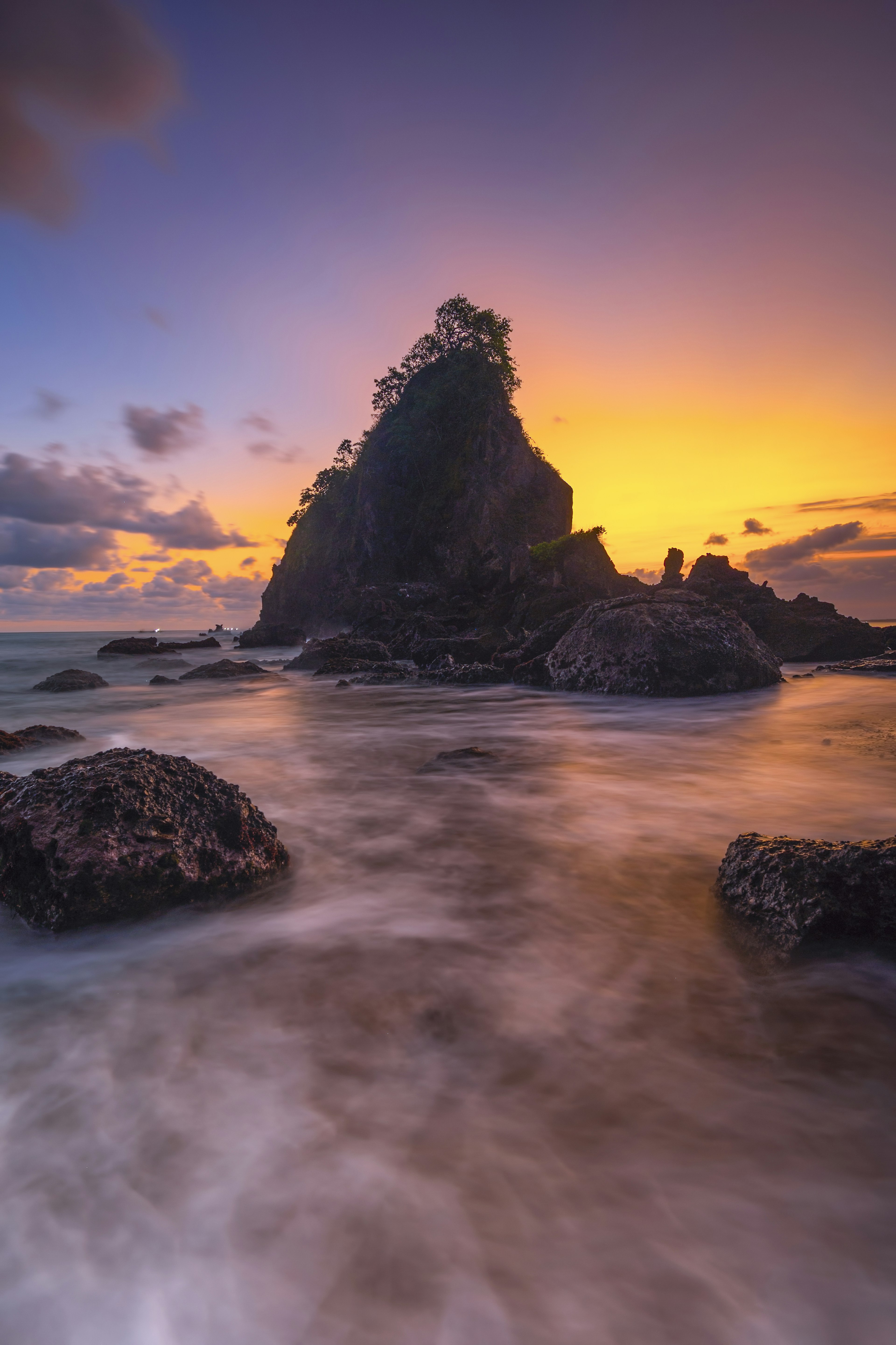 Batu besar di pantai saat matahari terbenam dengan ombak lembut