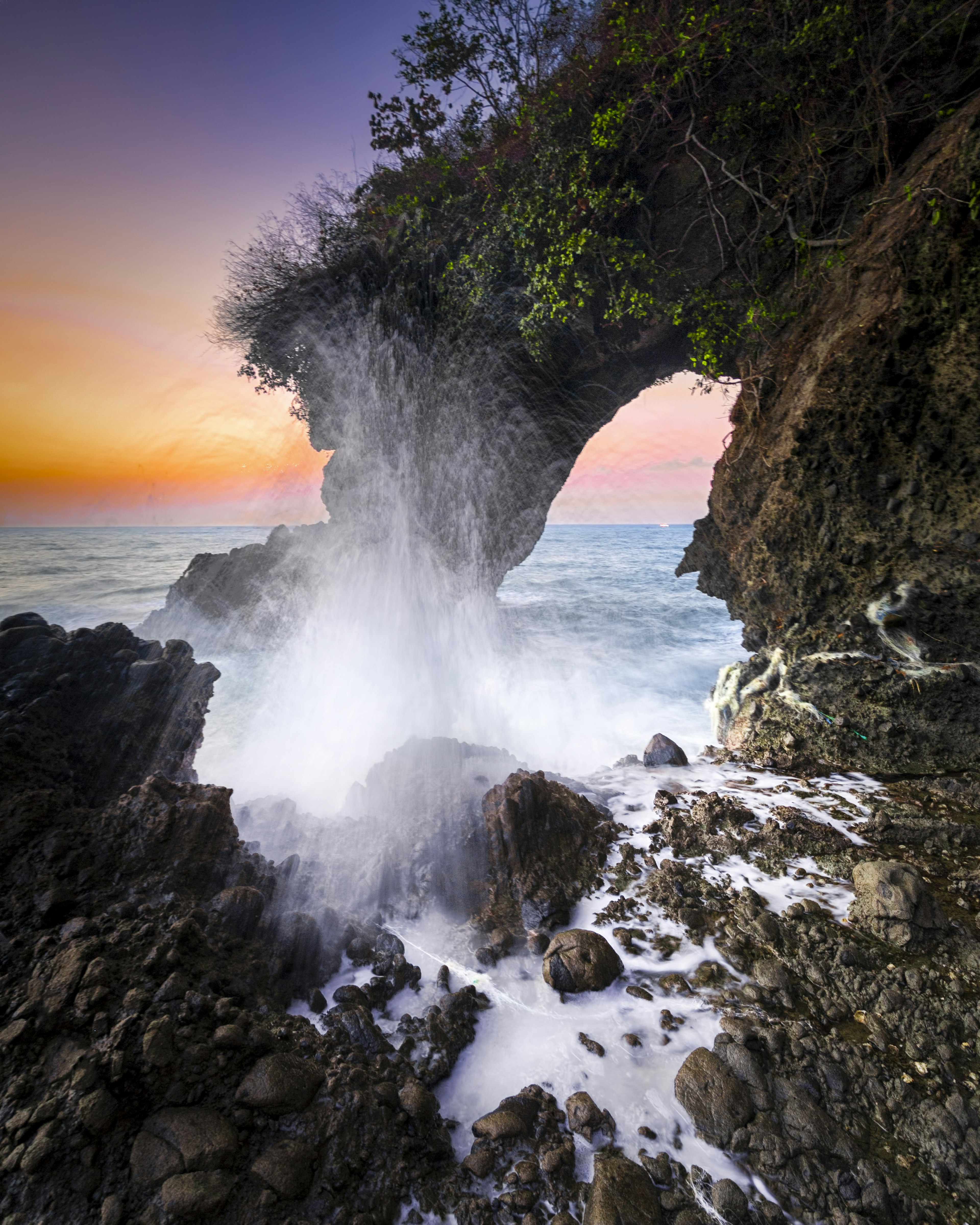 Pemandangan matahari terbenam yang menakjubkan dengan lengkungan batu dikelilingi ombak dan percikan