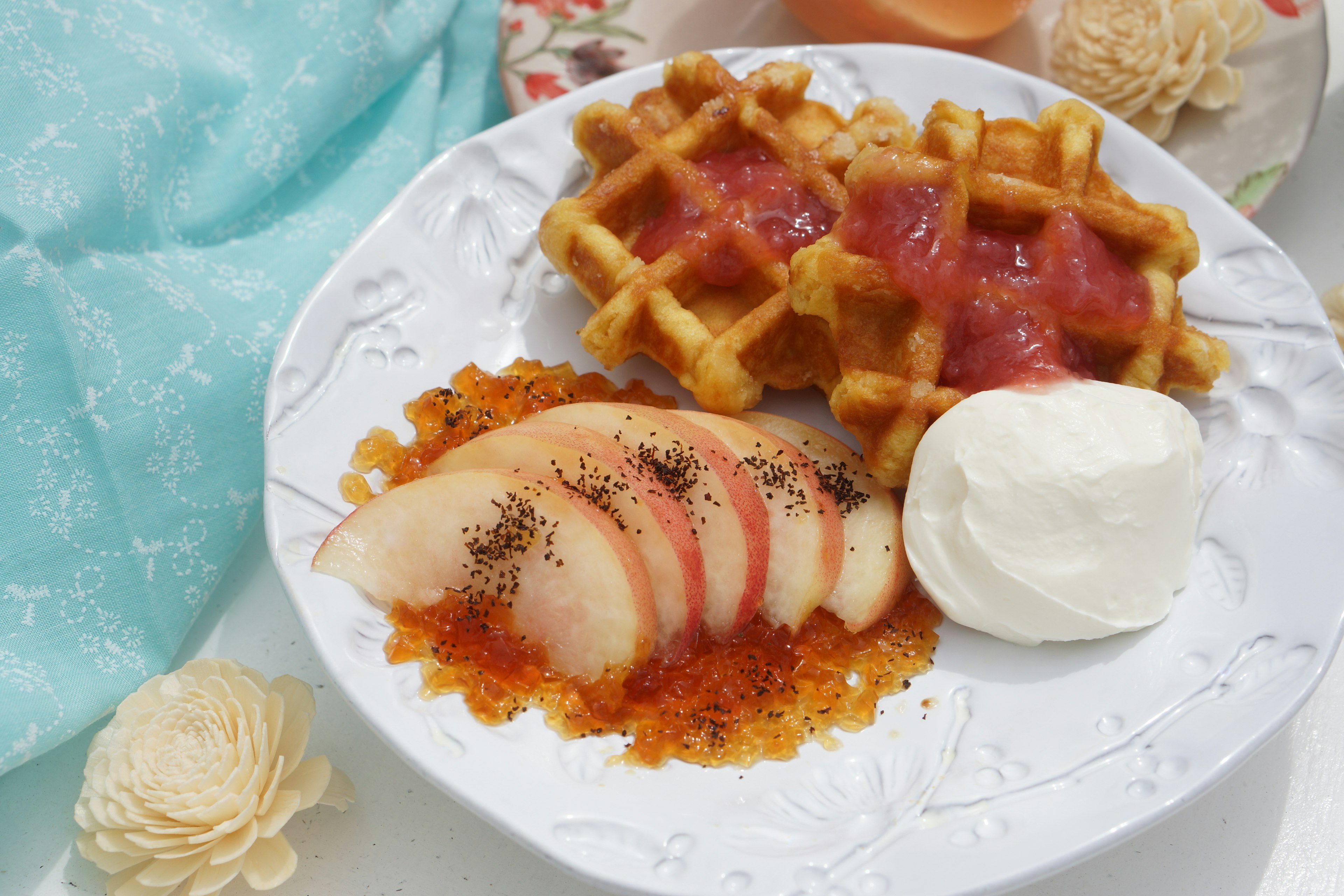 Plato de postre con melocotones en rodajas sobre un lecho de jarabe acompañado de waffles y crema