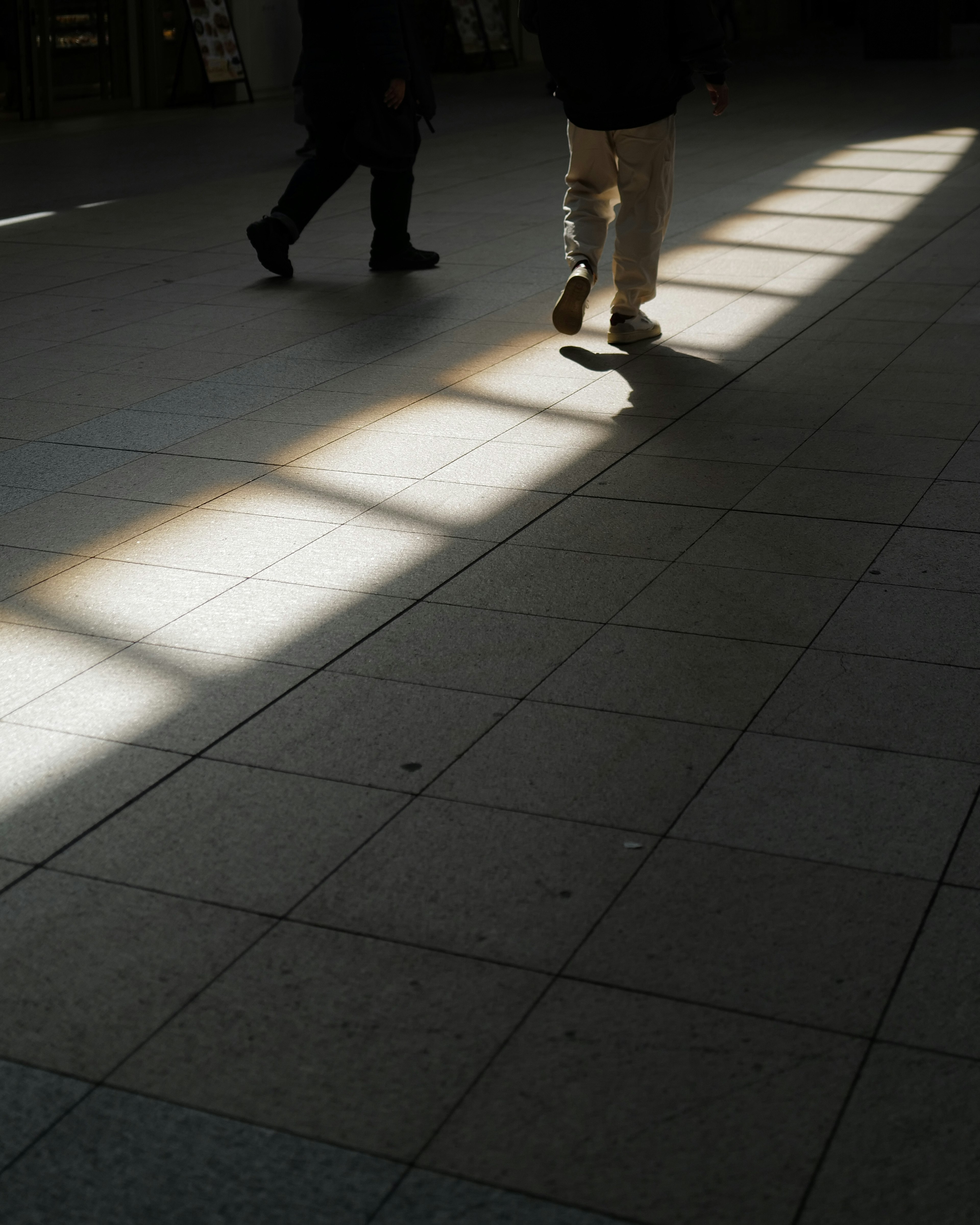 People walking in a space with tiled floor and intersecting light shadows