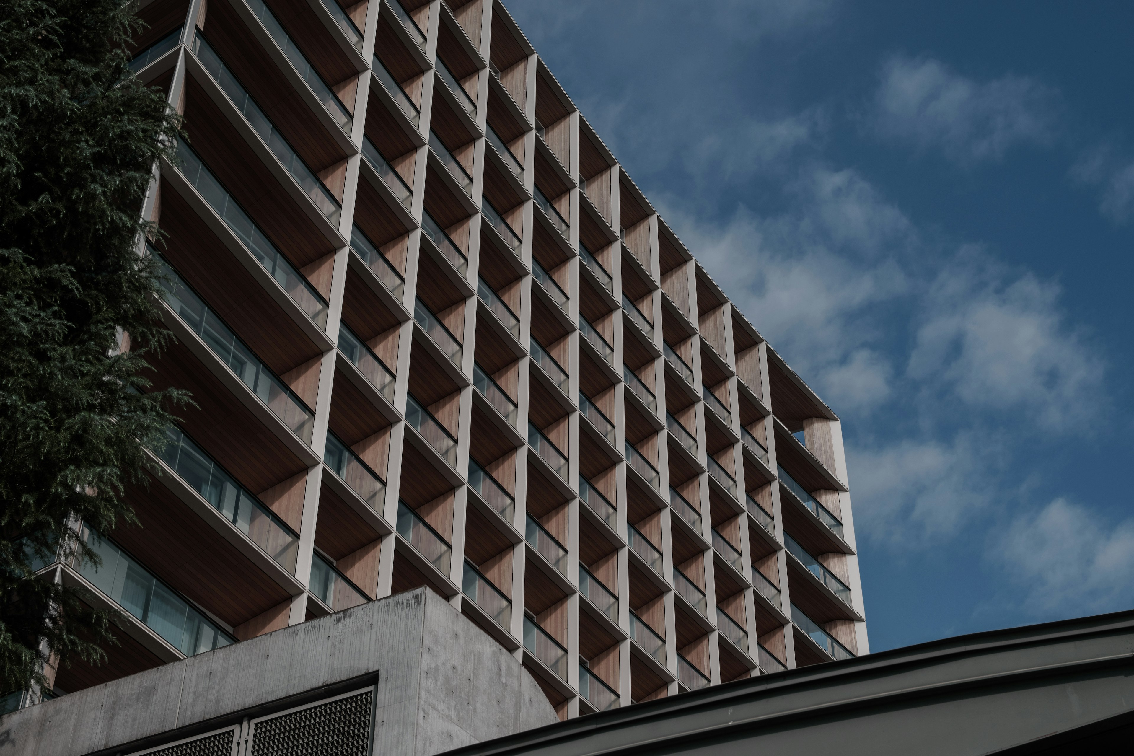 Façade d'un bâtiment moderne avec des motifs de fenêtres complexes sous un ciel bleu et des nuages