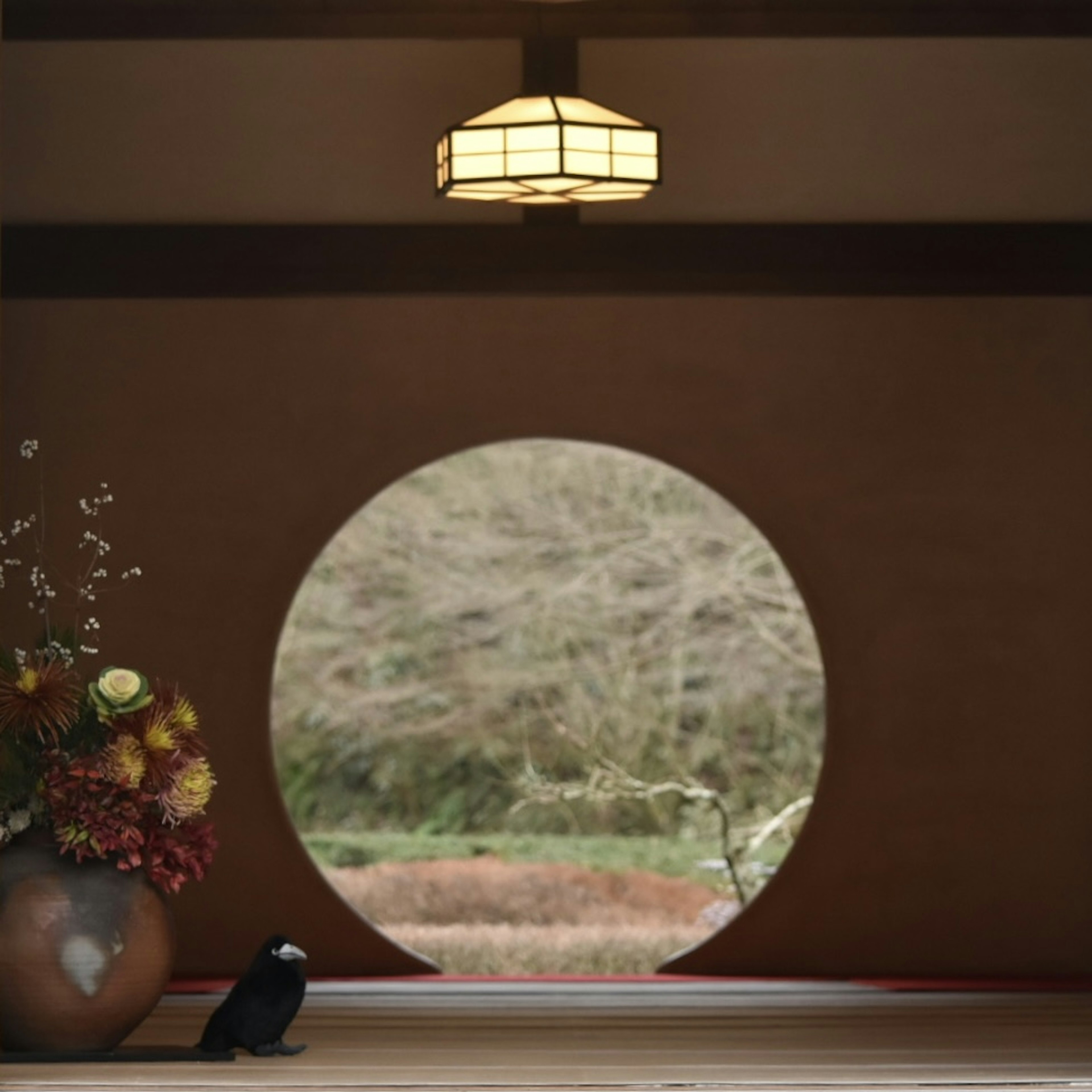 View through a round window showcasing nature and a vase of flowers