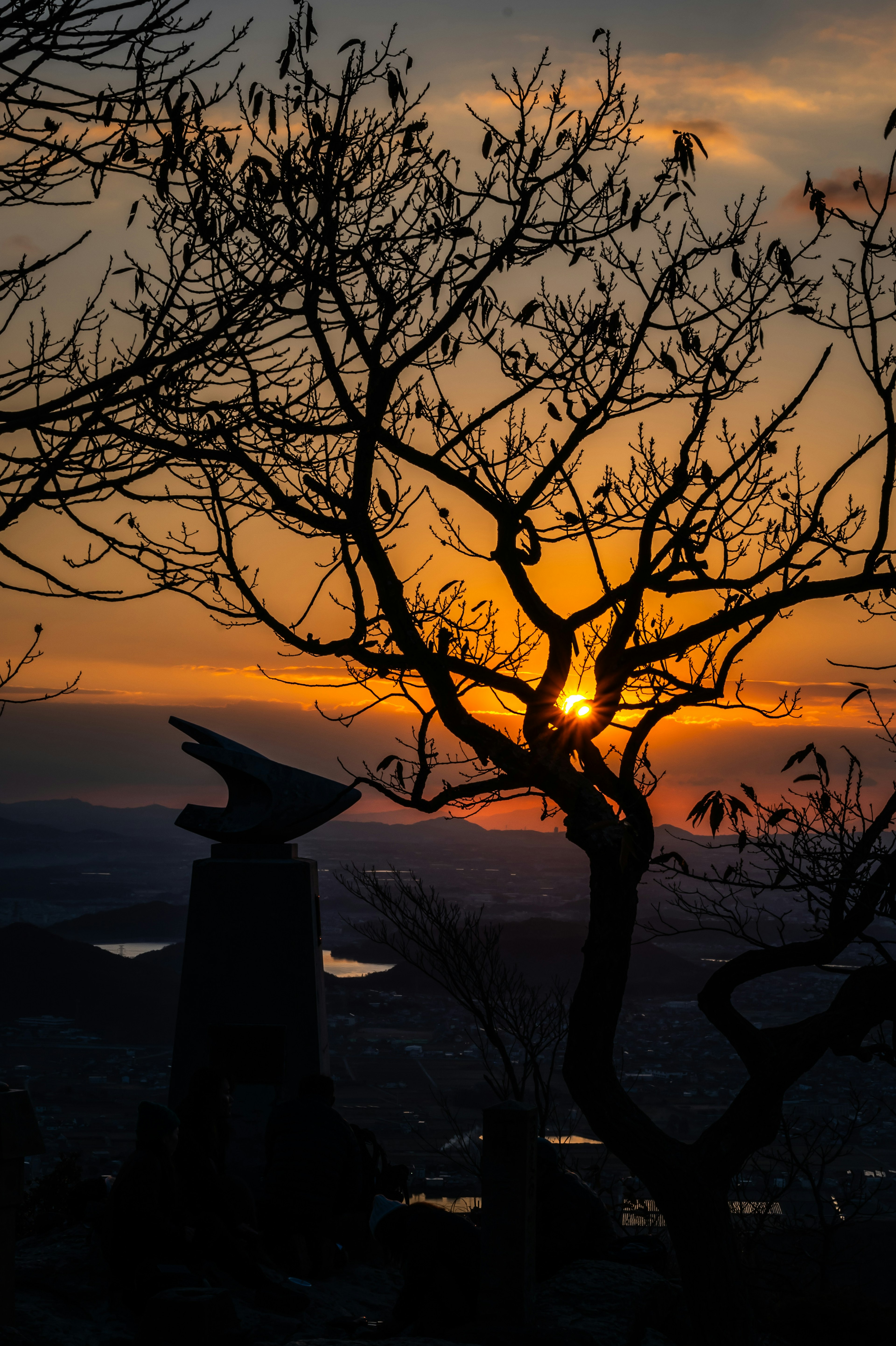 Silhouette eines Baumes und einer Steinstatue vor einem Sonnenuntergang