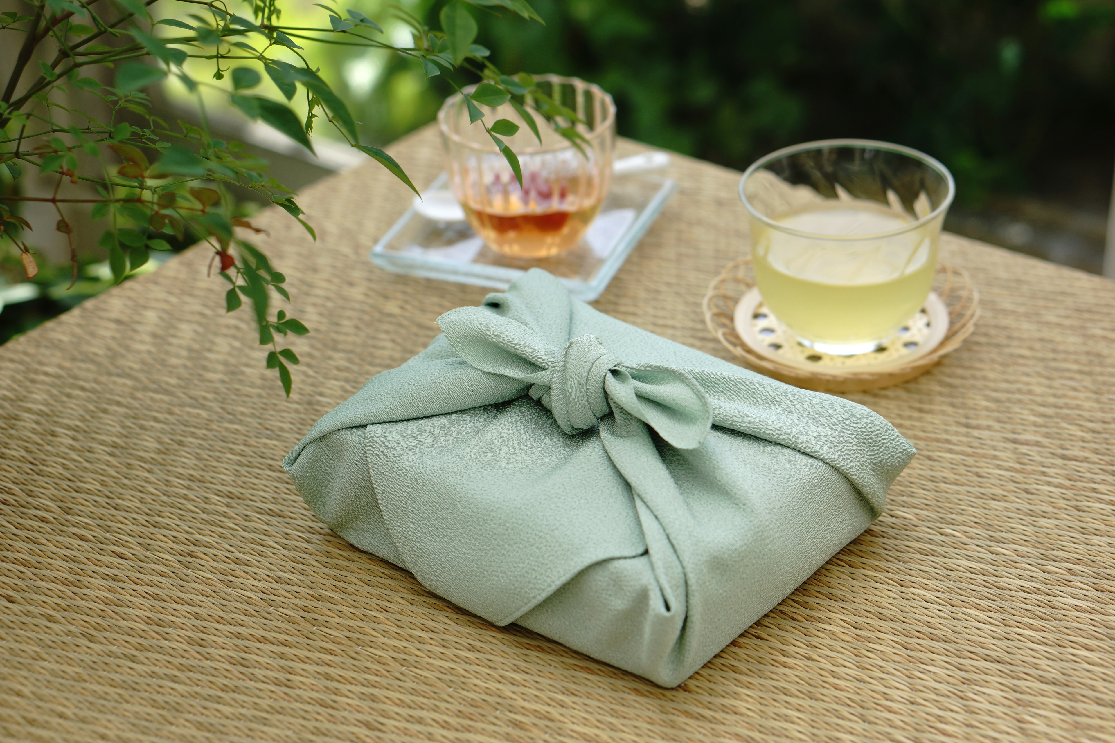 A gift wrapped in green fabric with tea and drinks on a table