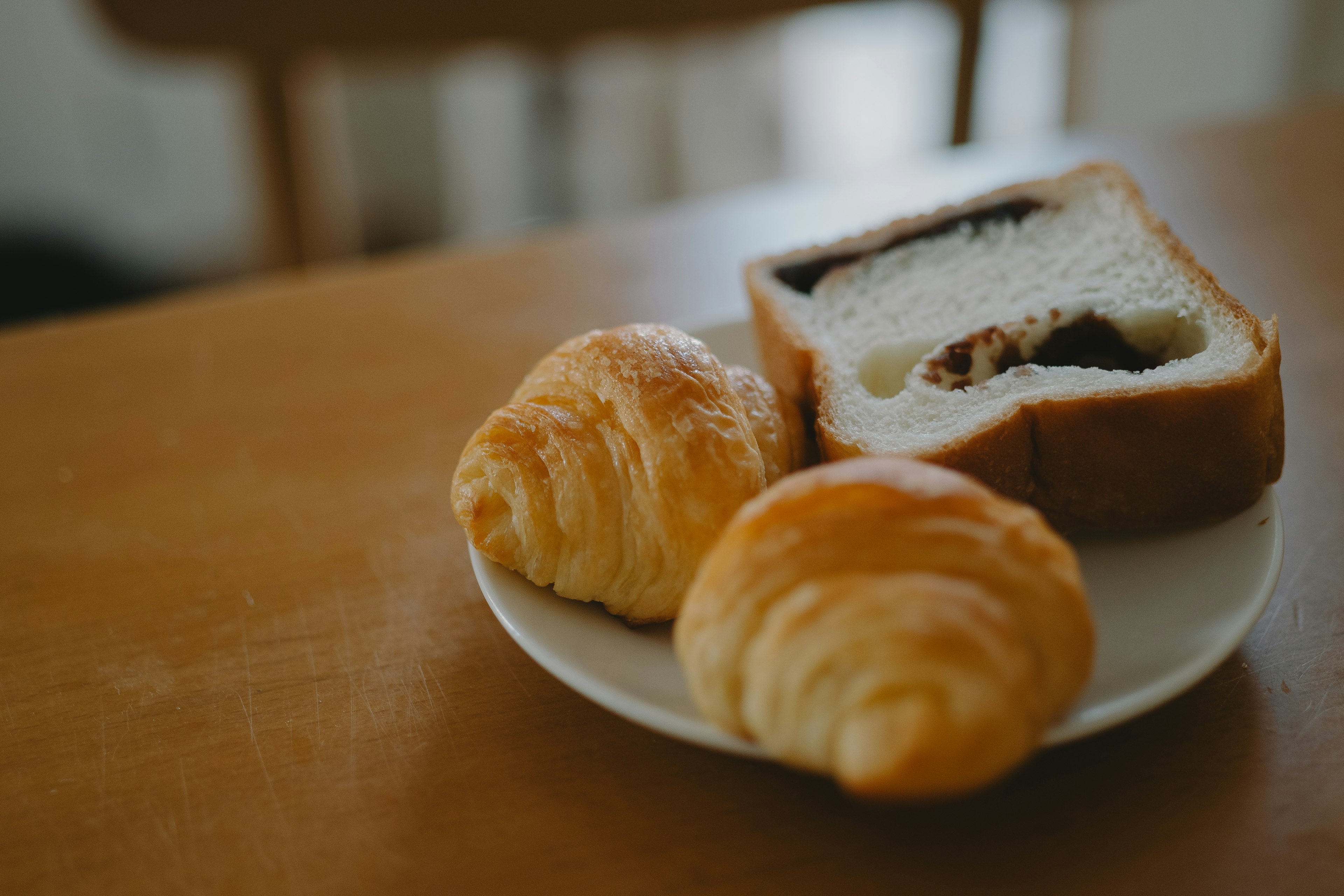 Croissants and a slice of bread on a plate on a wooden table