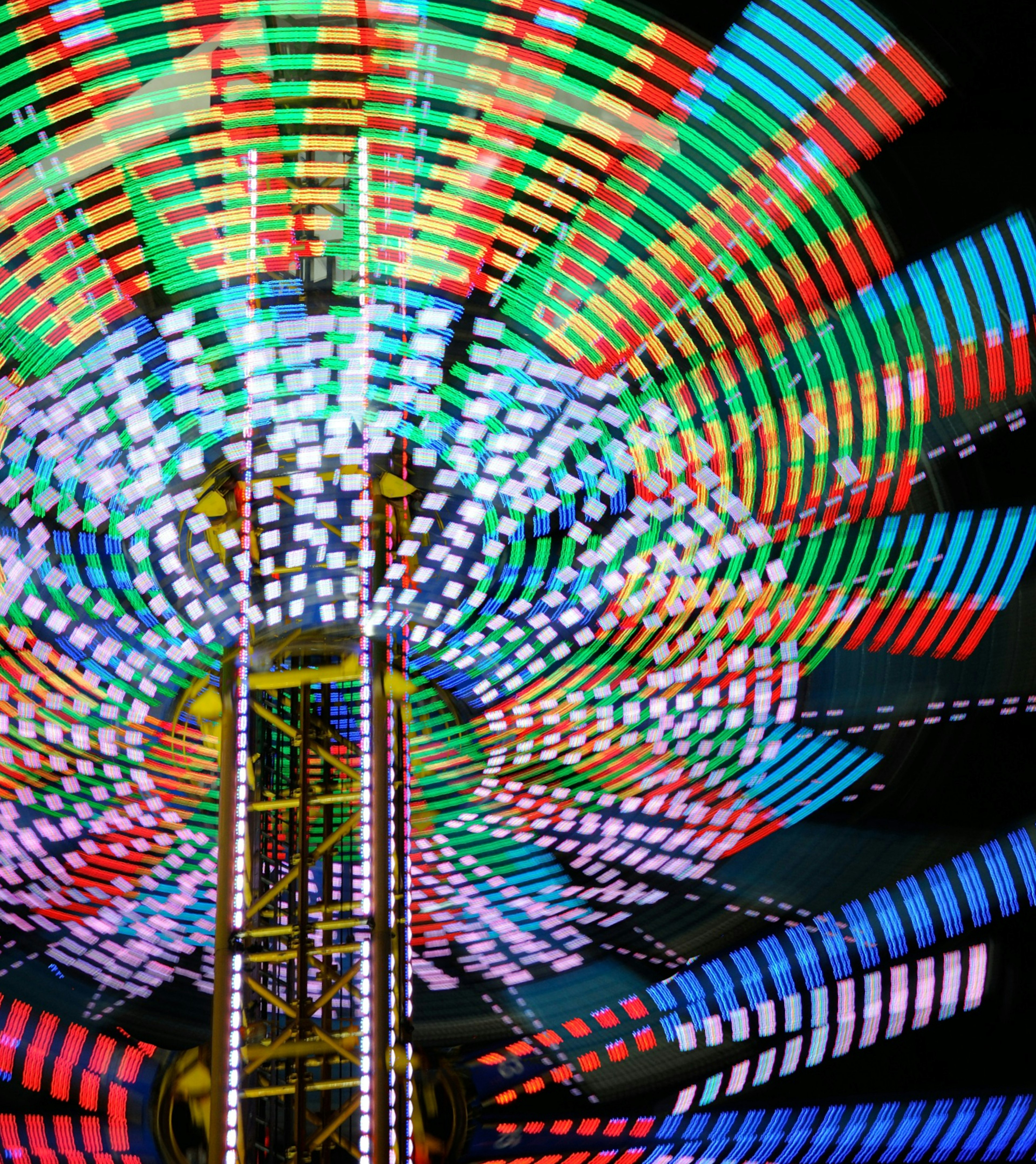 Bunte LED-Lichter einer sich drehenden Attraktion, die im Nachthimmel leuchten