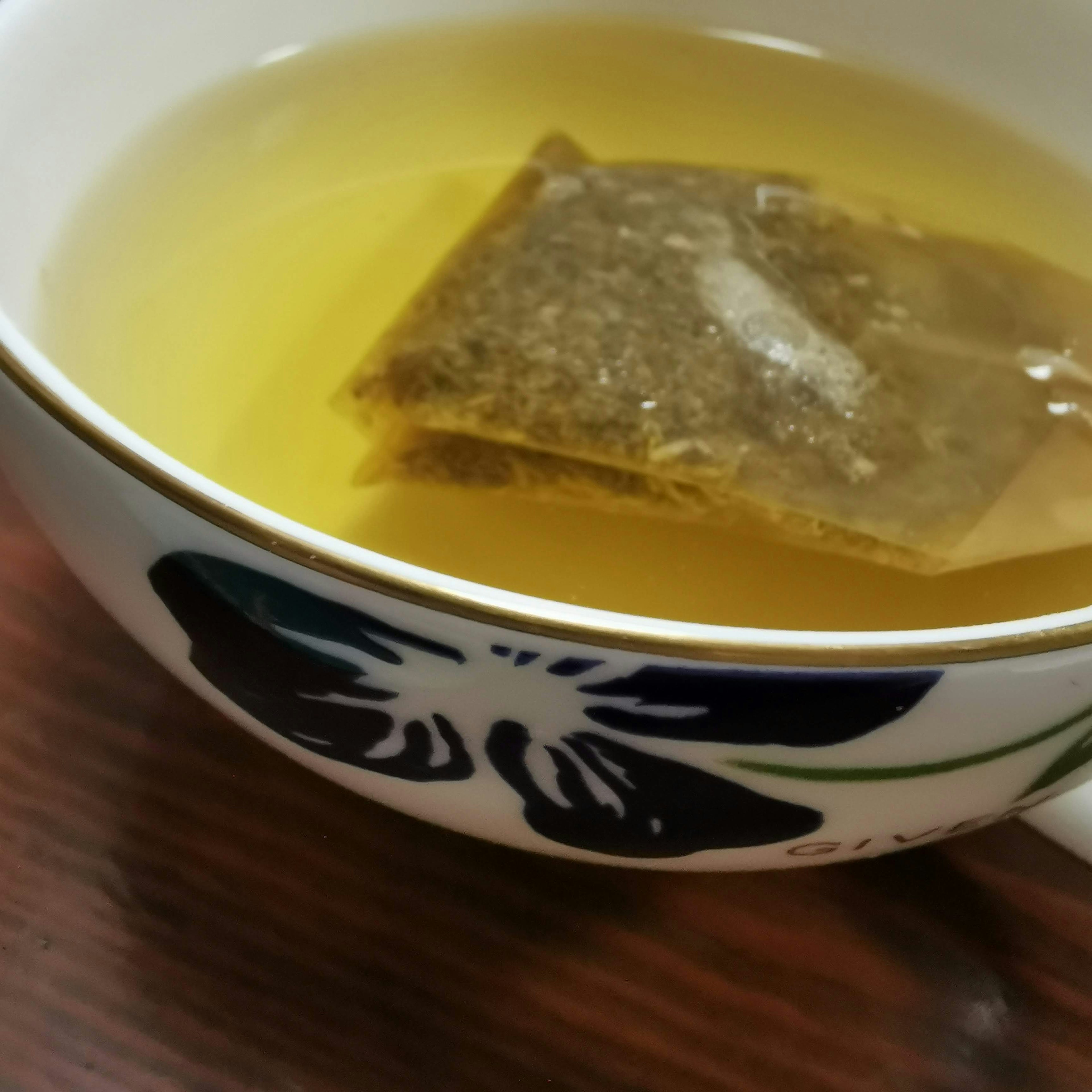 A cup of light green tea with a tea bag floating