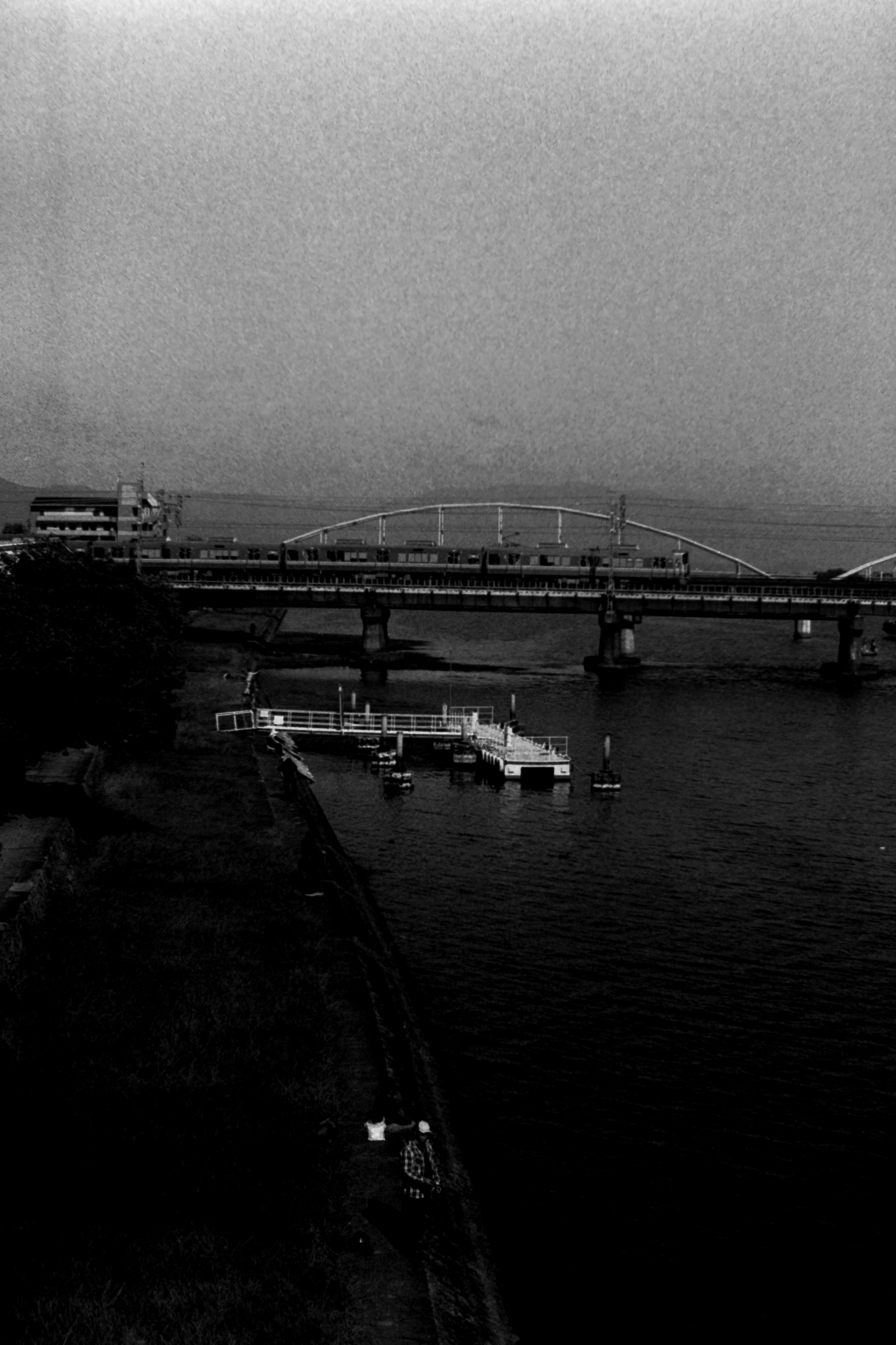 Scène de rivière en noir et blanc avec un pont et des bateaux