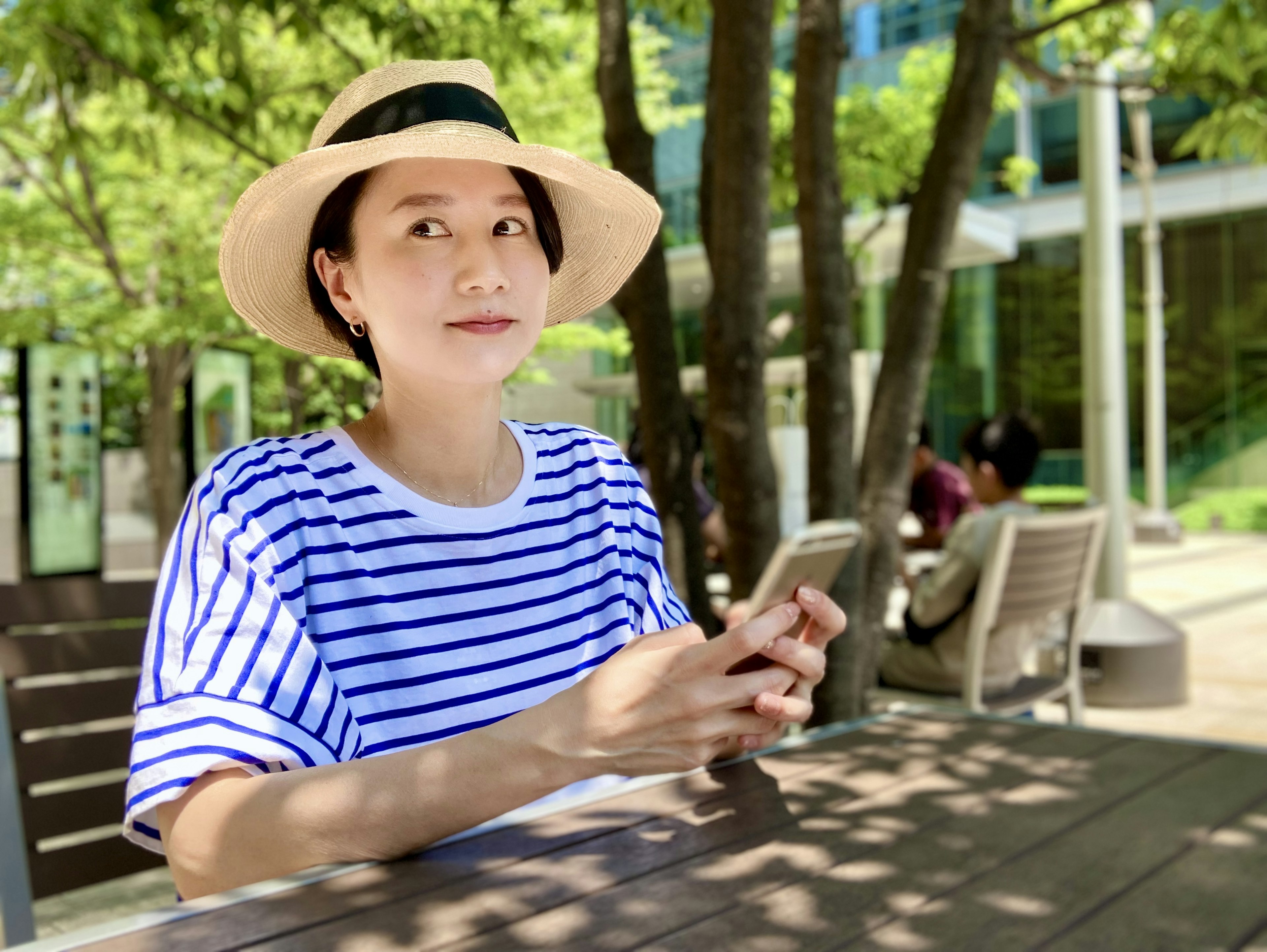 A woman sitting at an outdoor table wearing a striped shirt and hat with a relaxed expression