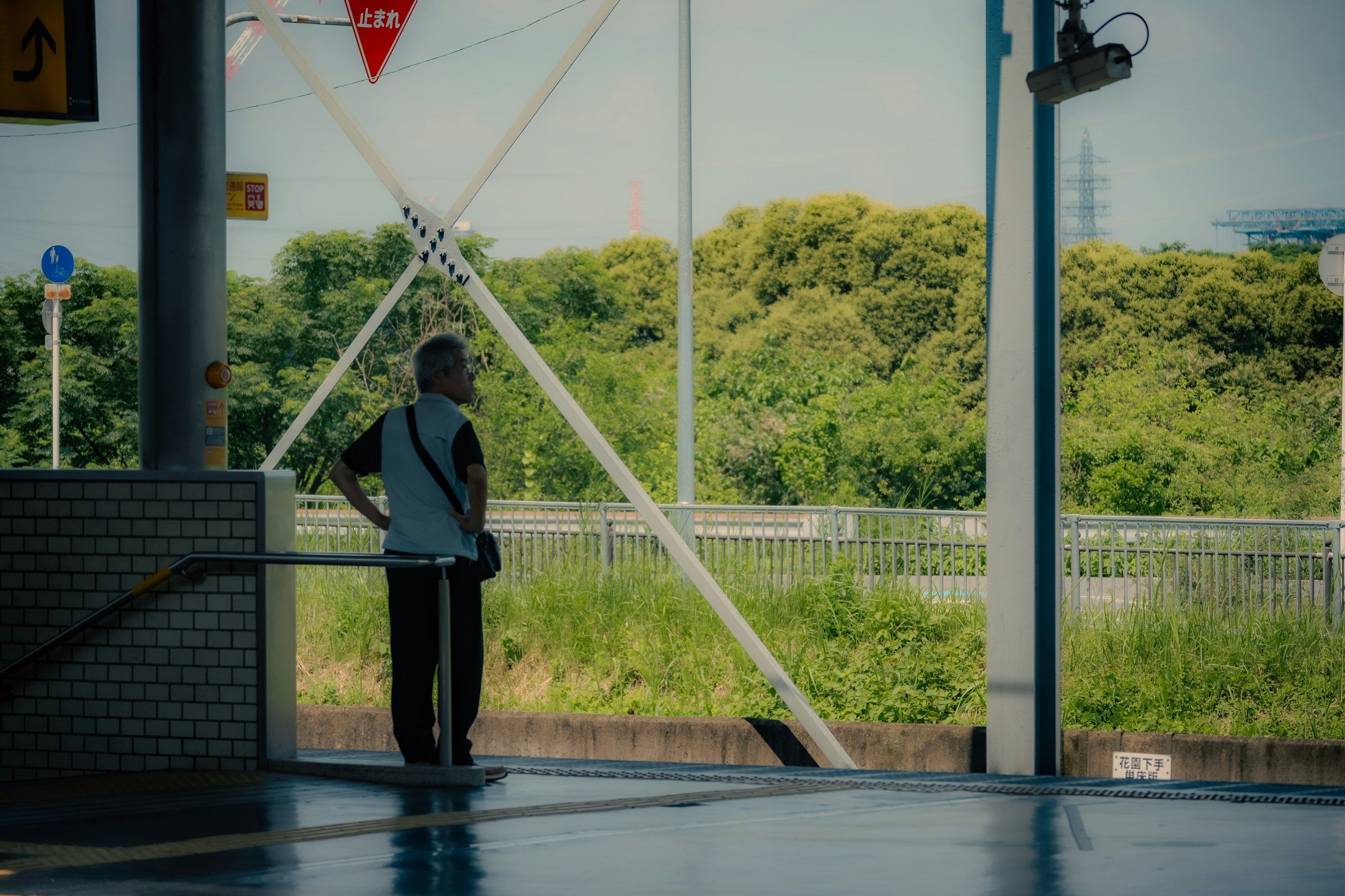 駅のプラットフォームで待っている男性の後ろ姿 緑の風景が背景に広がる