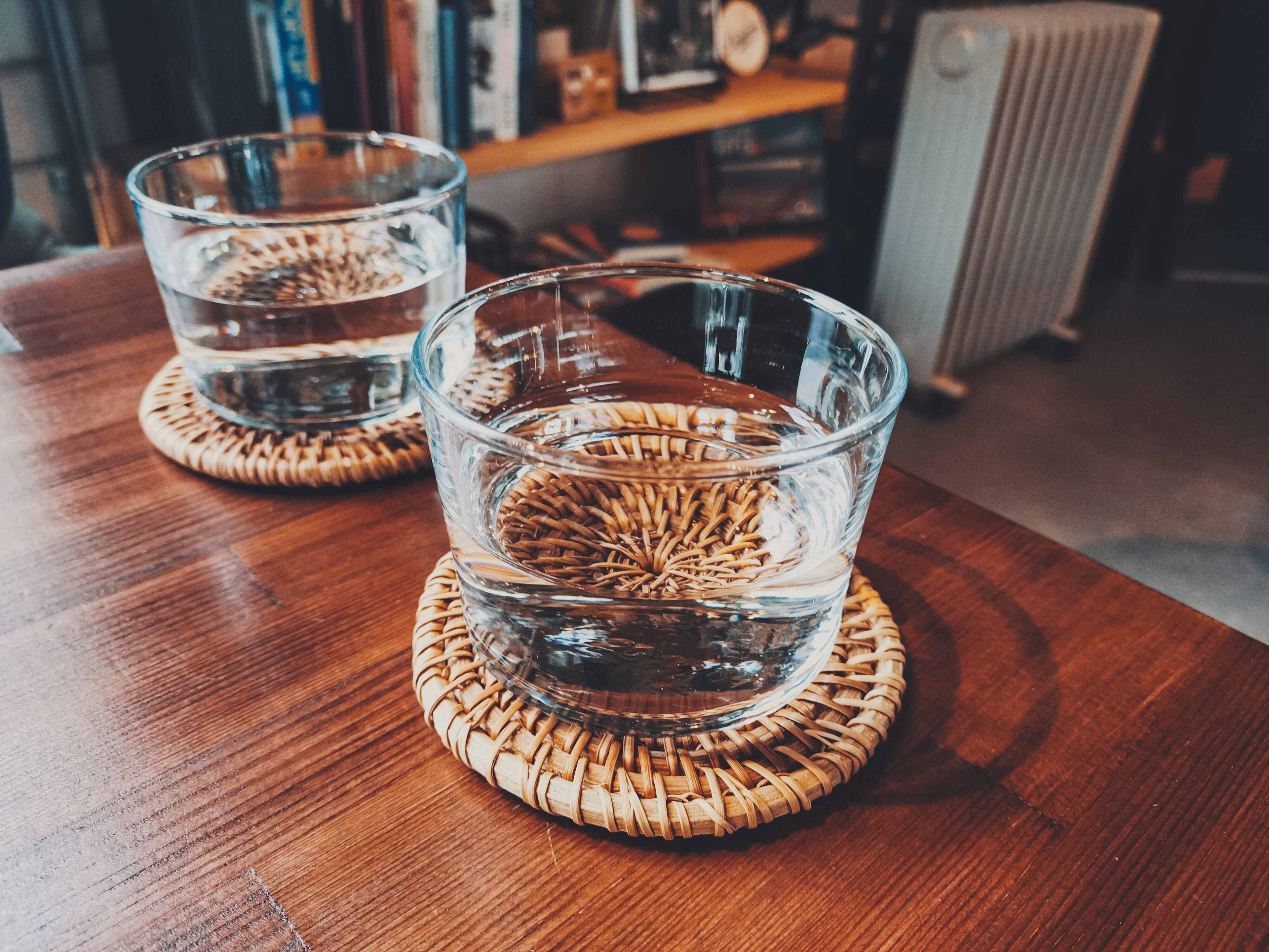 Two glasses of water on woven coasters placed on a wooden table