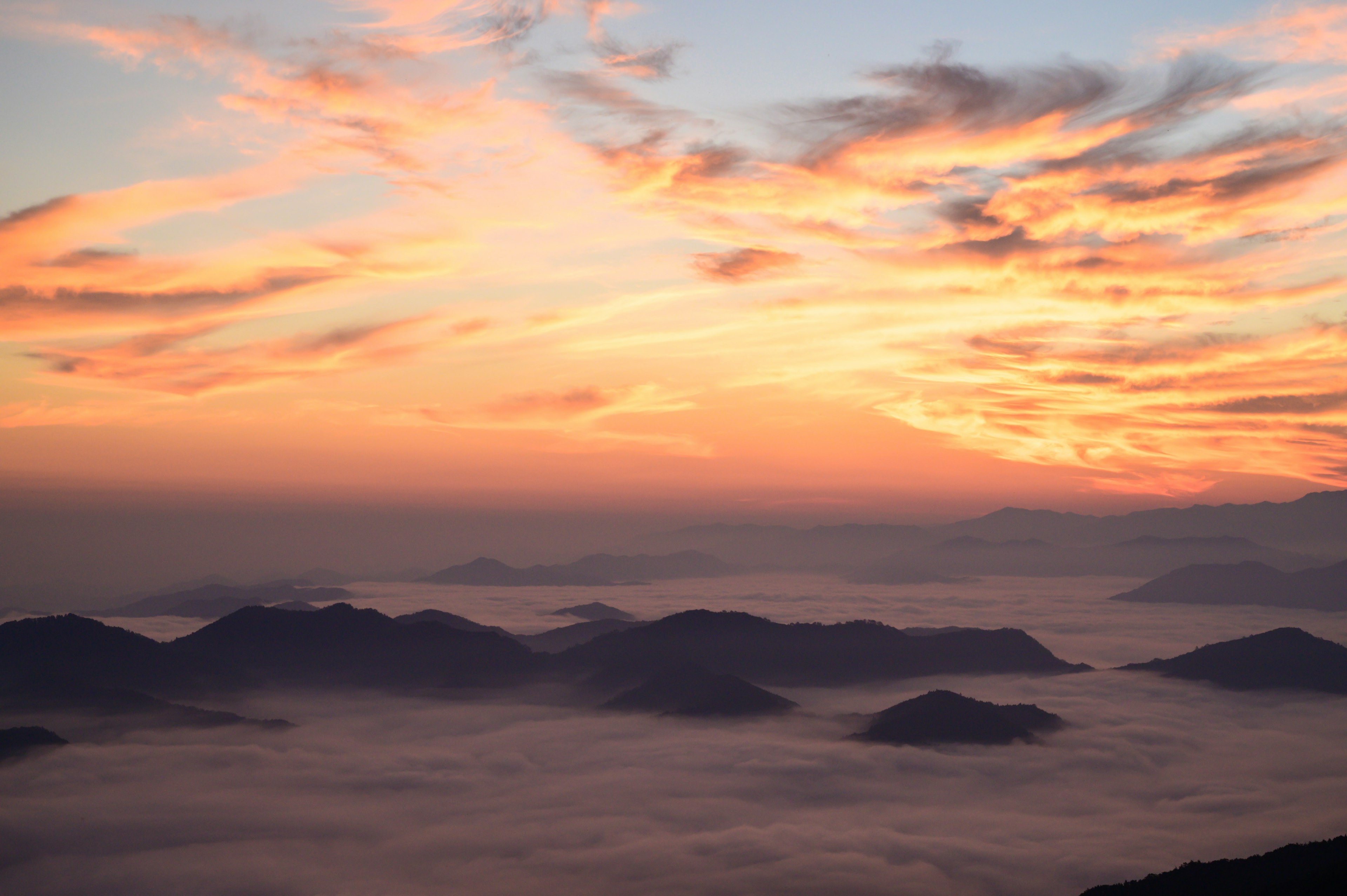 Pemandangan pegunungan yang tertutup kabut dengan langit matahari terbenam yang cerah