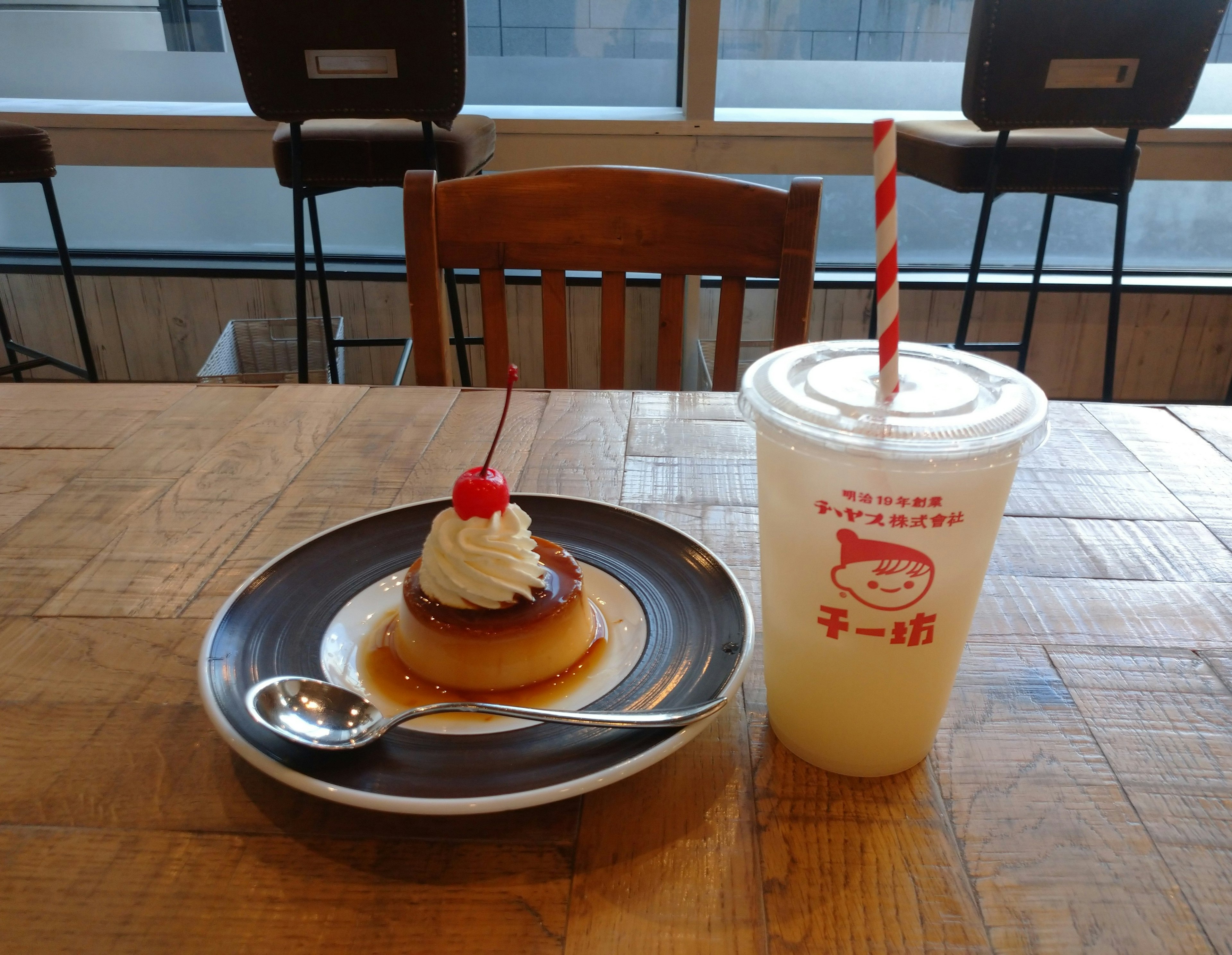 Image of a pudding dessert on a plate with whipped cream and cherry topped next to a drink in a cup