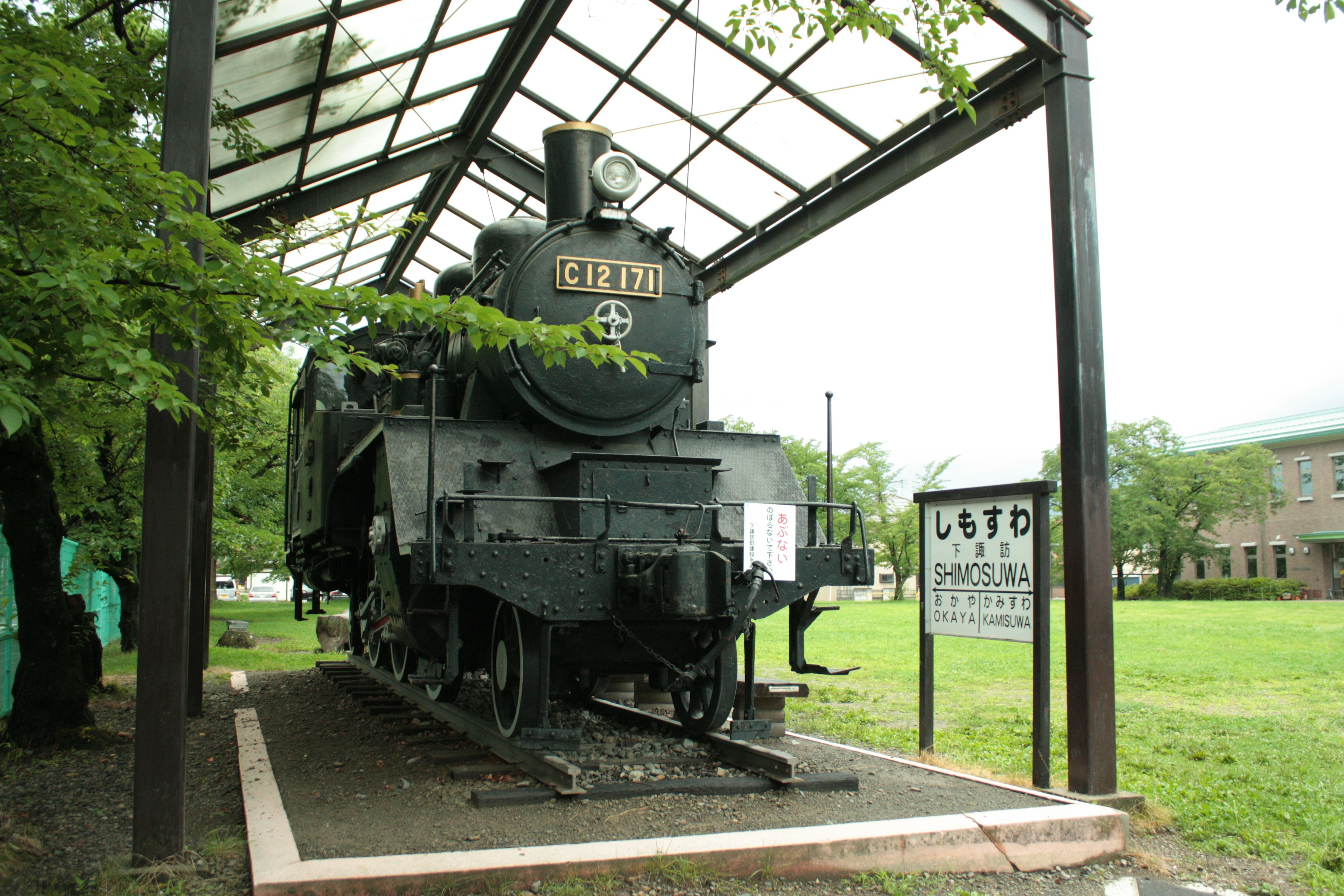 Exposición de una locomotora de vapor bajo una estructura techada rodeada de césped verde