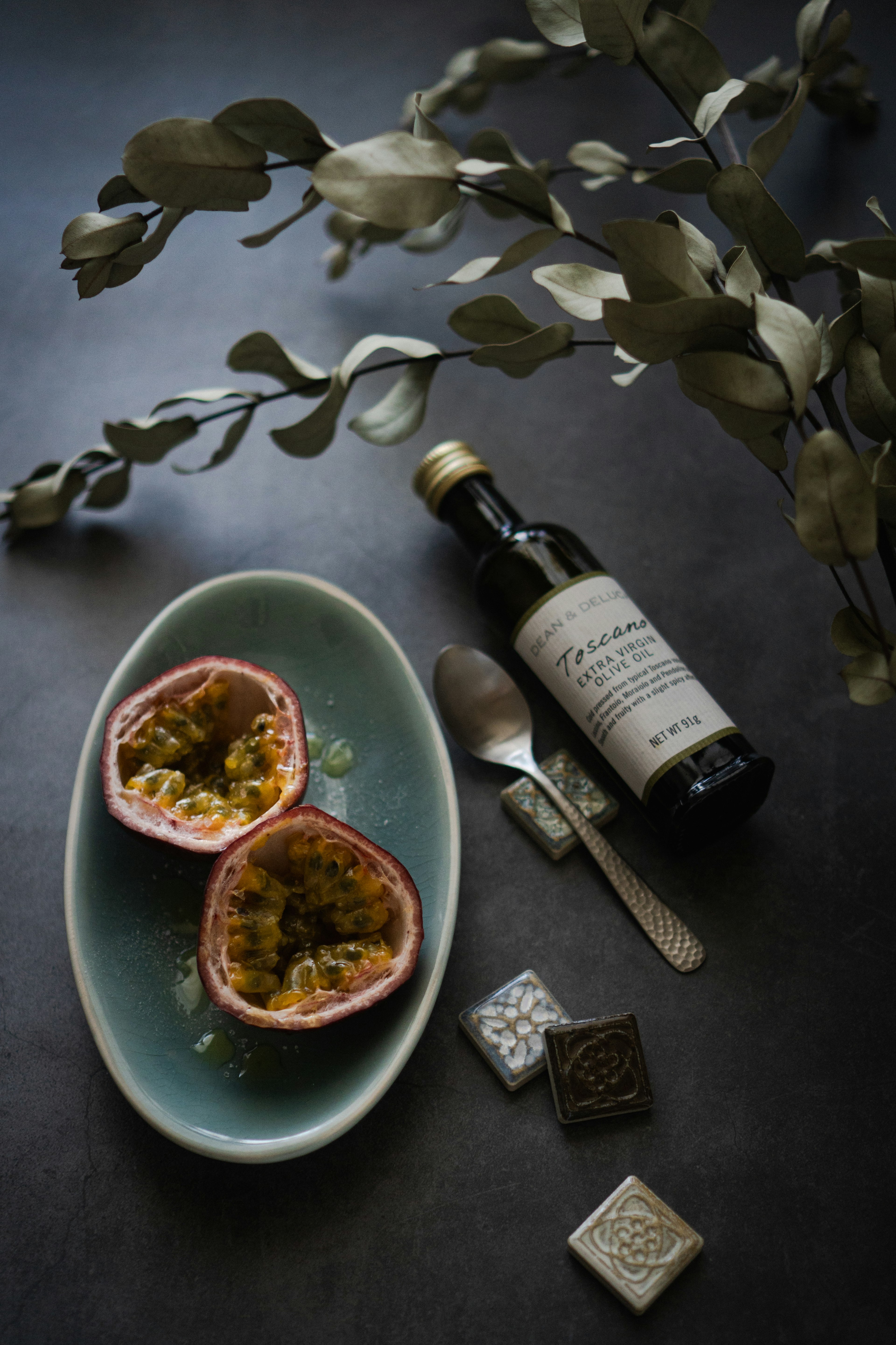 Passion fruit halved on a blue plate with a spoon and an oil bottle alongside decorative leaves