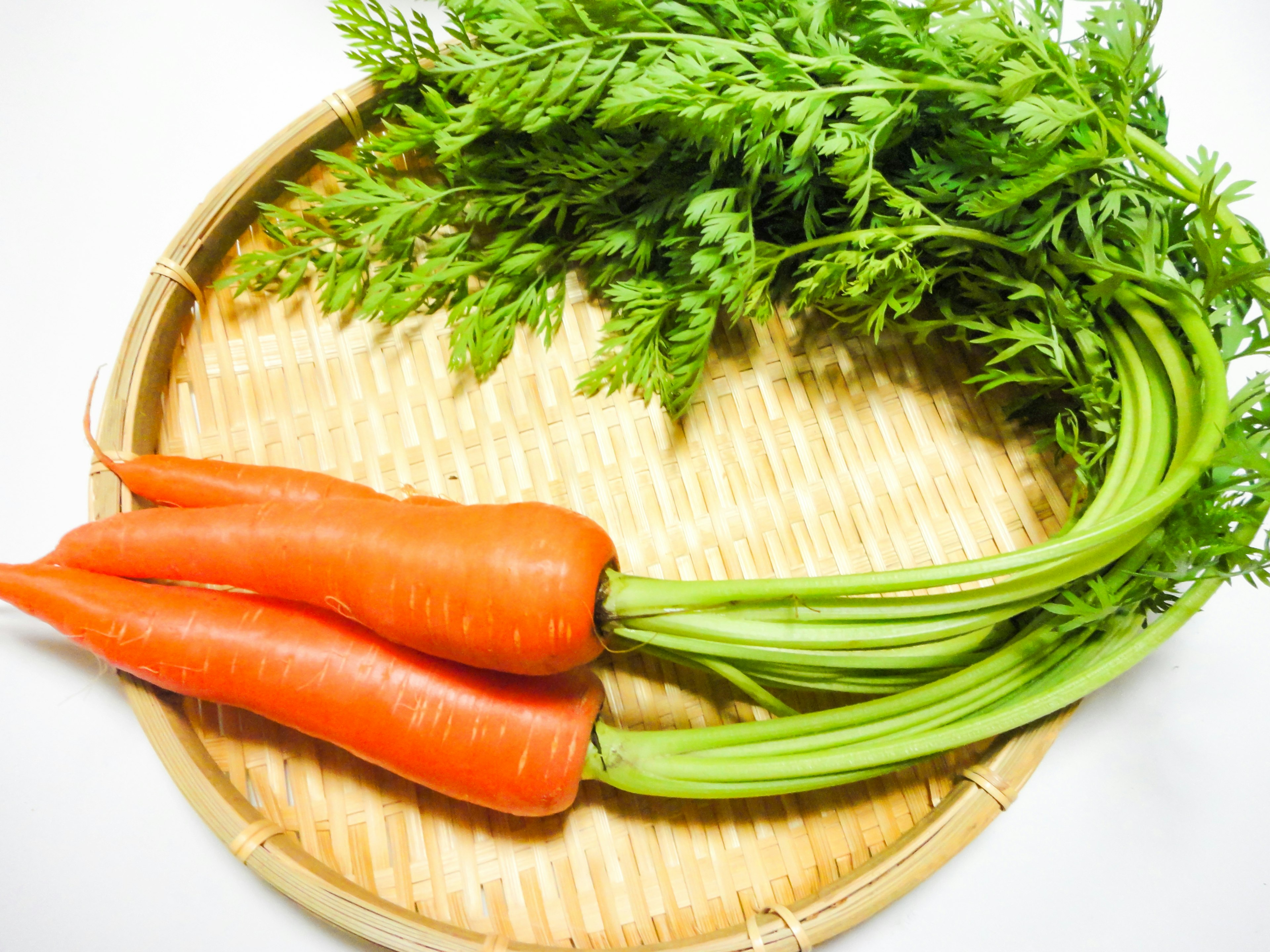 Fresh carrots with green tops on a woven basket