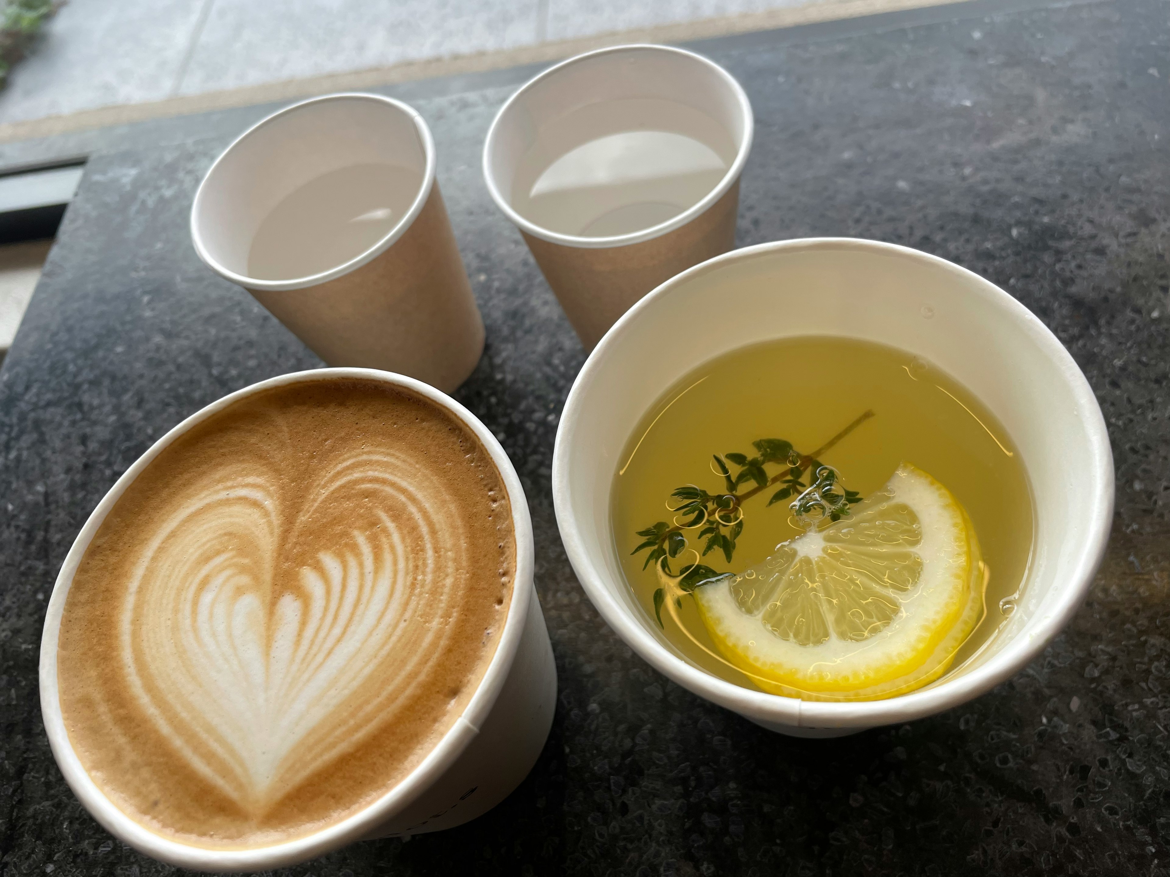 Café con arte latte en forma de corazón y una bebida con rodaja de limón y hierbas