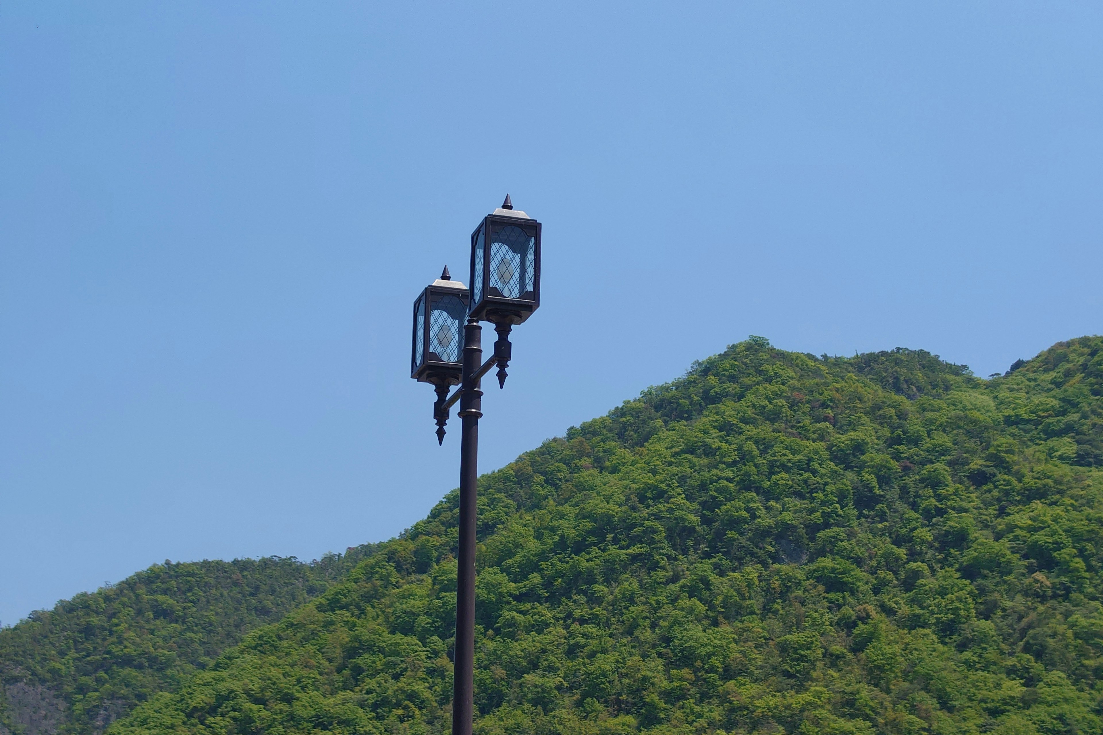 Deux lampadaires de style lanterne devant un fond de montagnes verdoyantes sous un ciel bleu clair