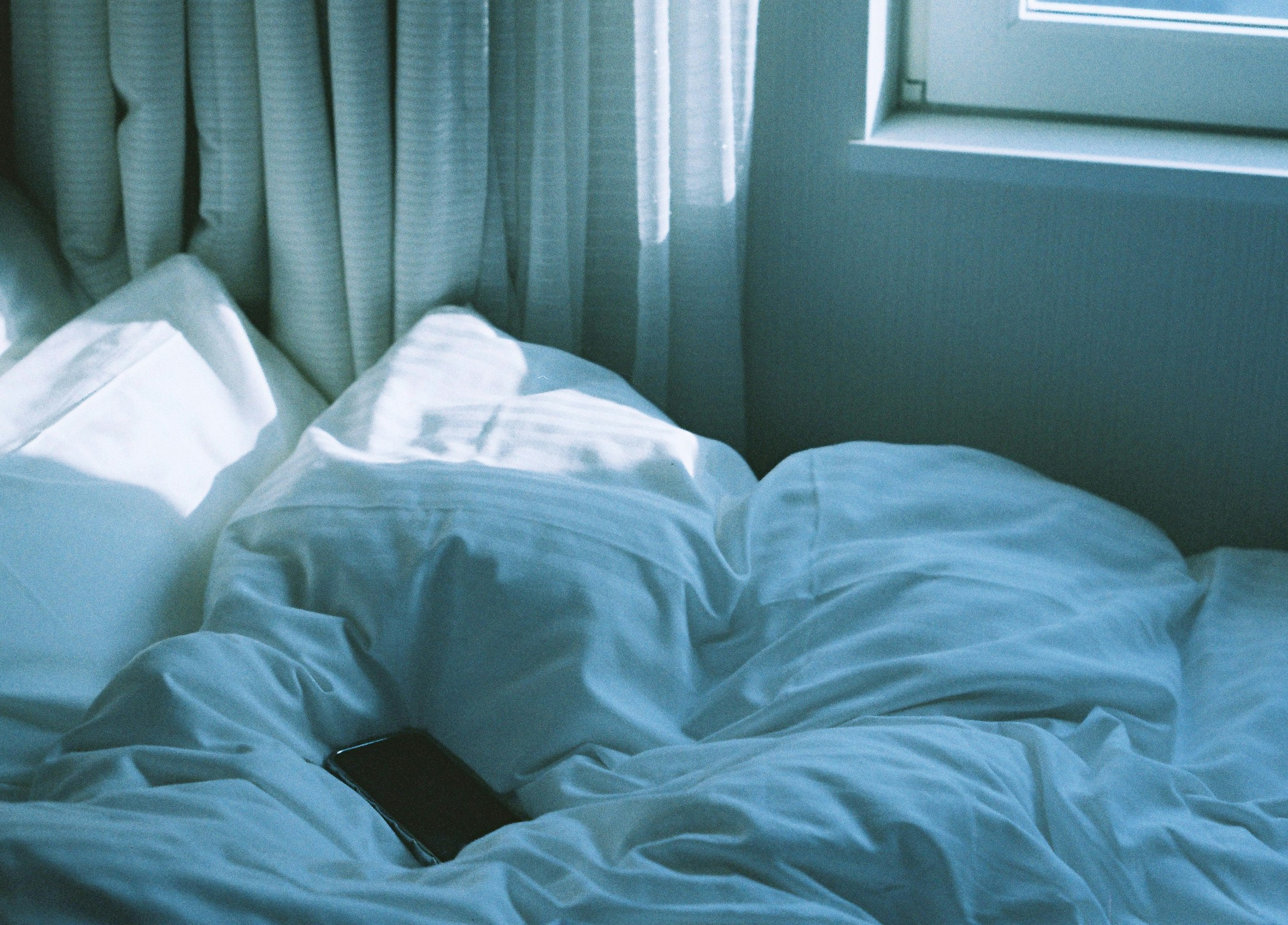 Esquina brillante de un dormitorio con ropa de cama blanca suave y cortinas