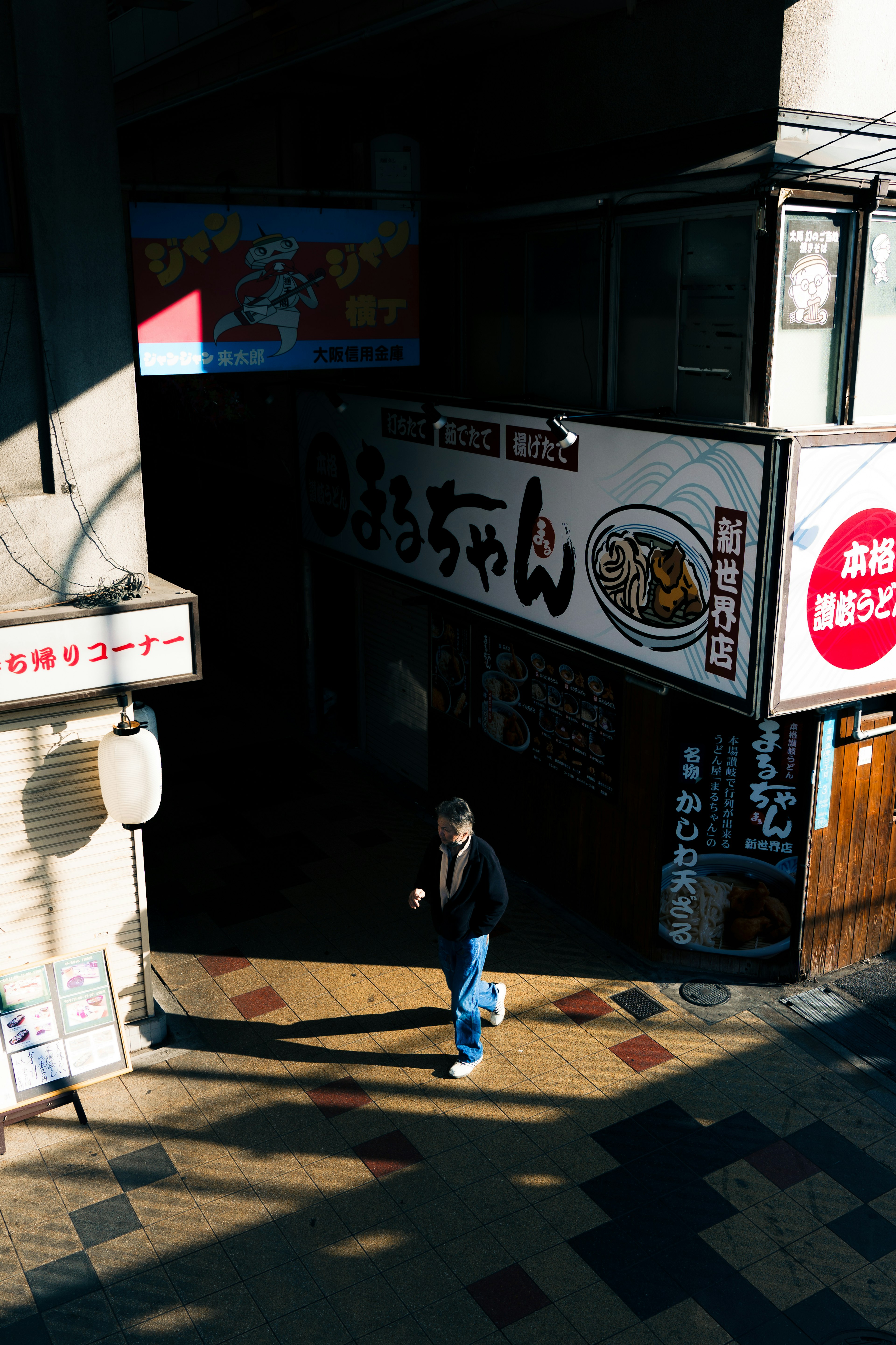 Street scene with a person walking, prominent signage, sunlight casting shadows