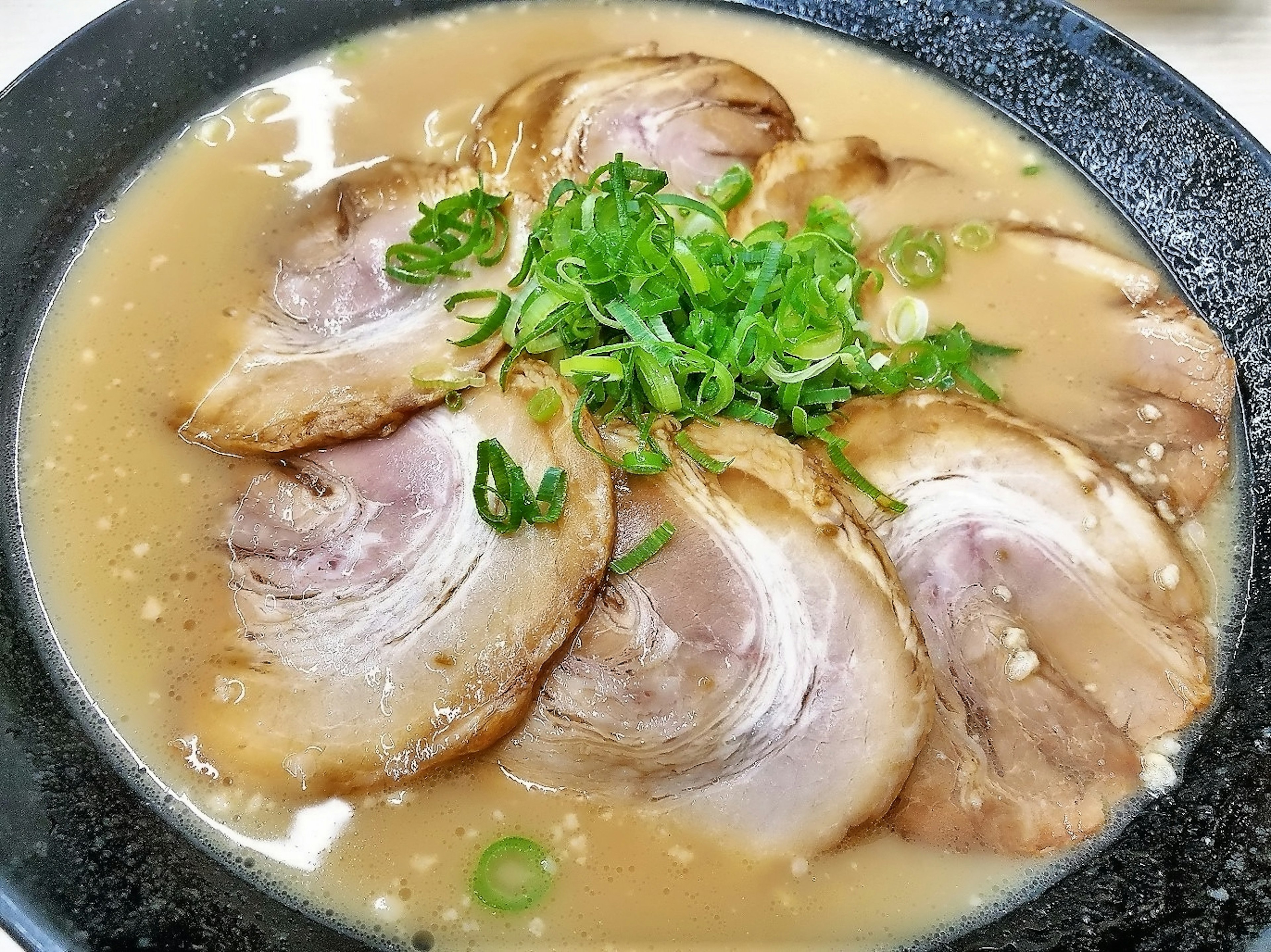 Bol de ramen tonkotsu avec des tranches de chashu et des oignons verts