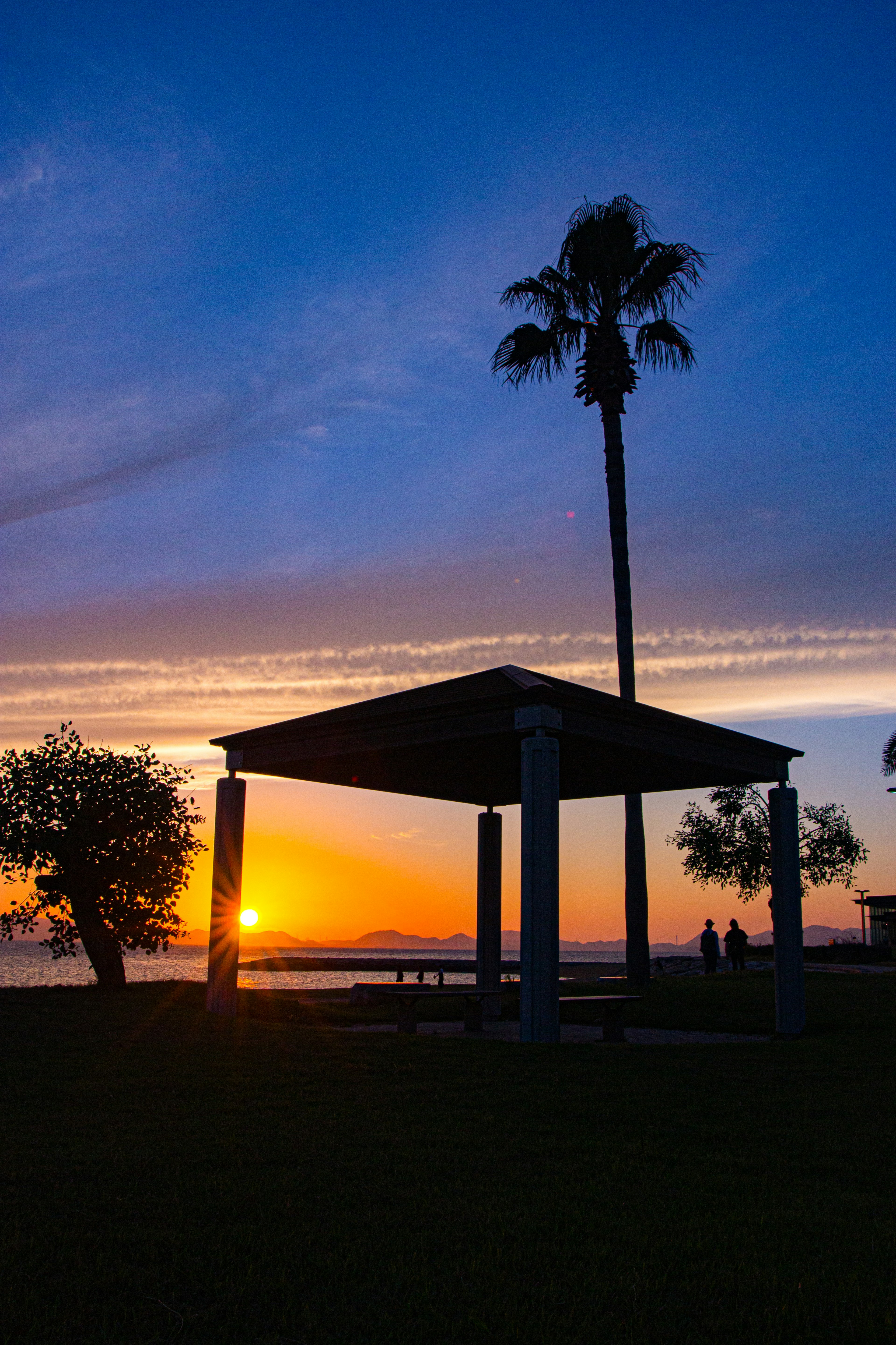 Silhouette of a gazebo and palm tree against a colorful sunset