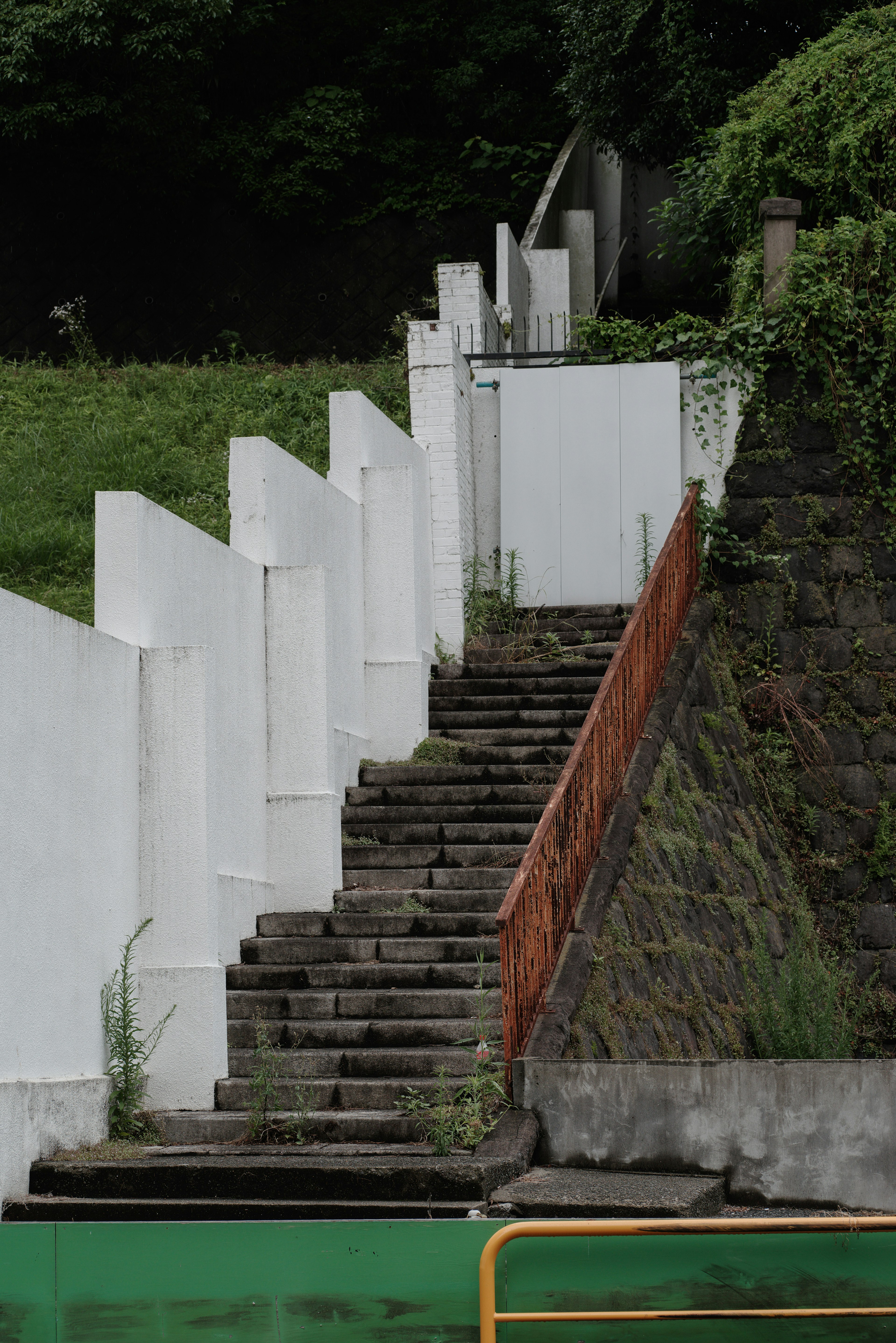 Escalera con muros blancos rodeada de vegetación y muro de piedra