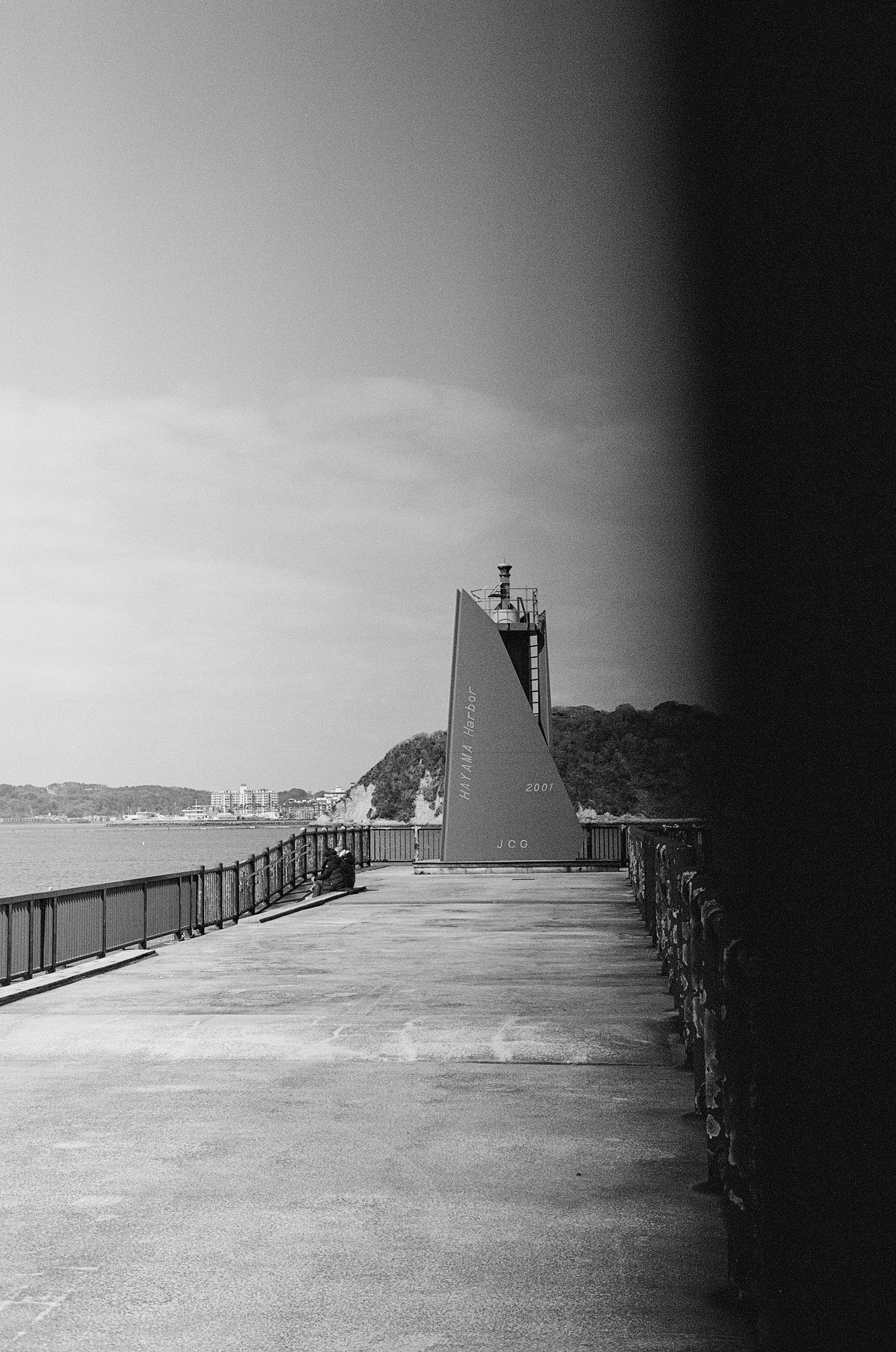 海岸沿いのコンクリートの道と独特な形の塔がある白黒の風景