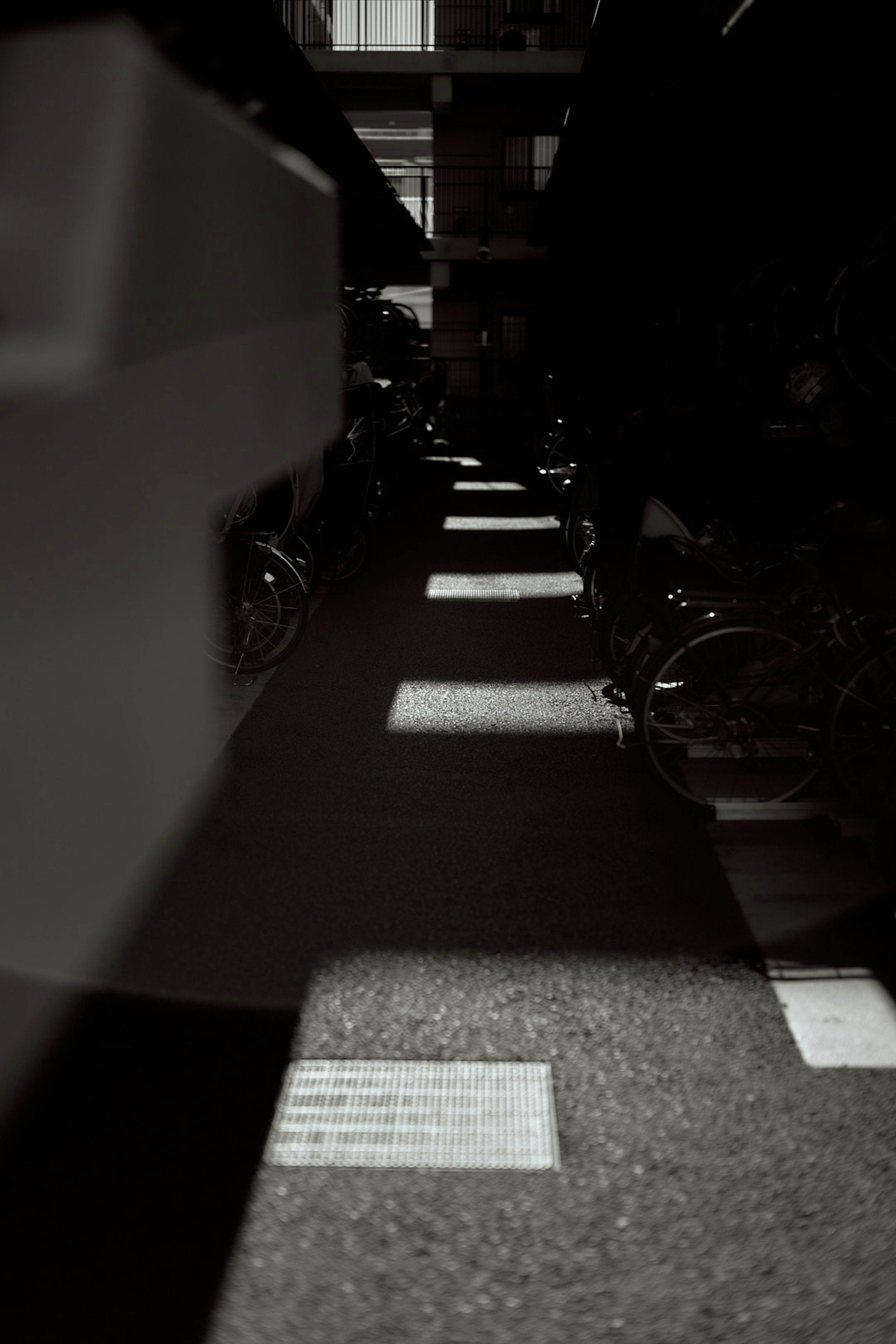 A dimly lit alley with shadows cast on the ground and bicycles parked along the sides