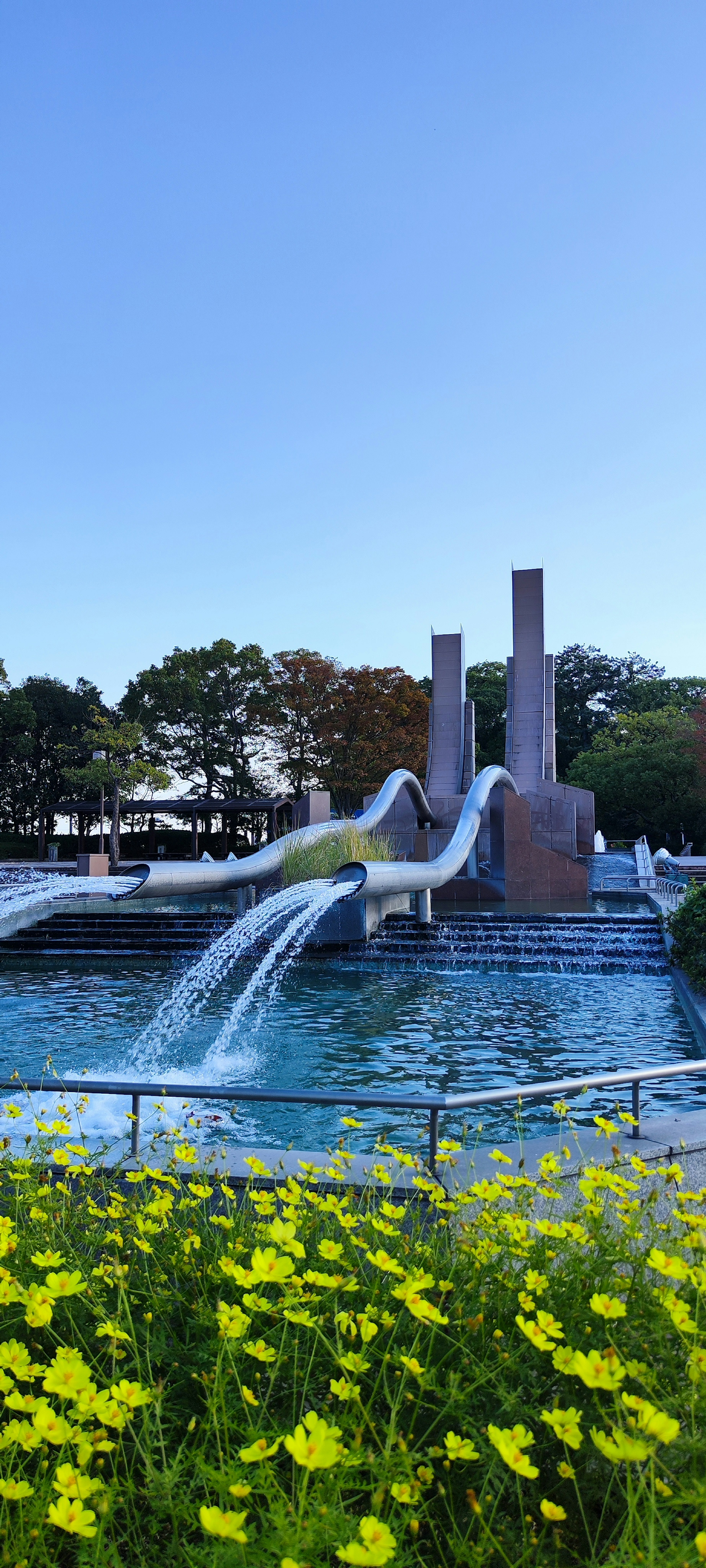 Fontaine avec de l'eau qui coule et des fleurs jaunes sous un ciel bleu clair