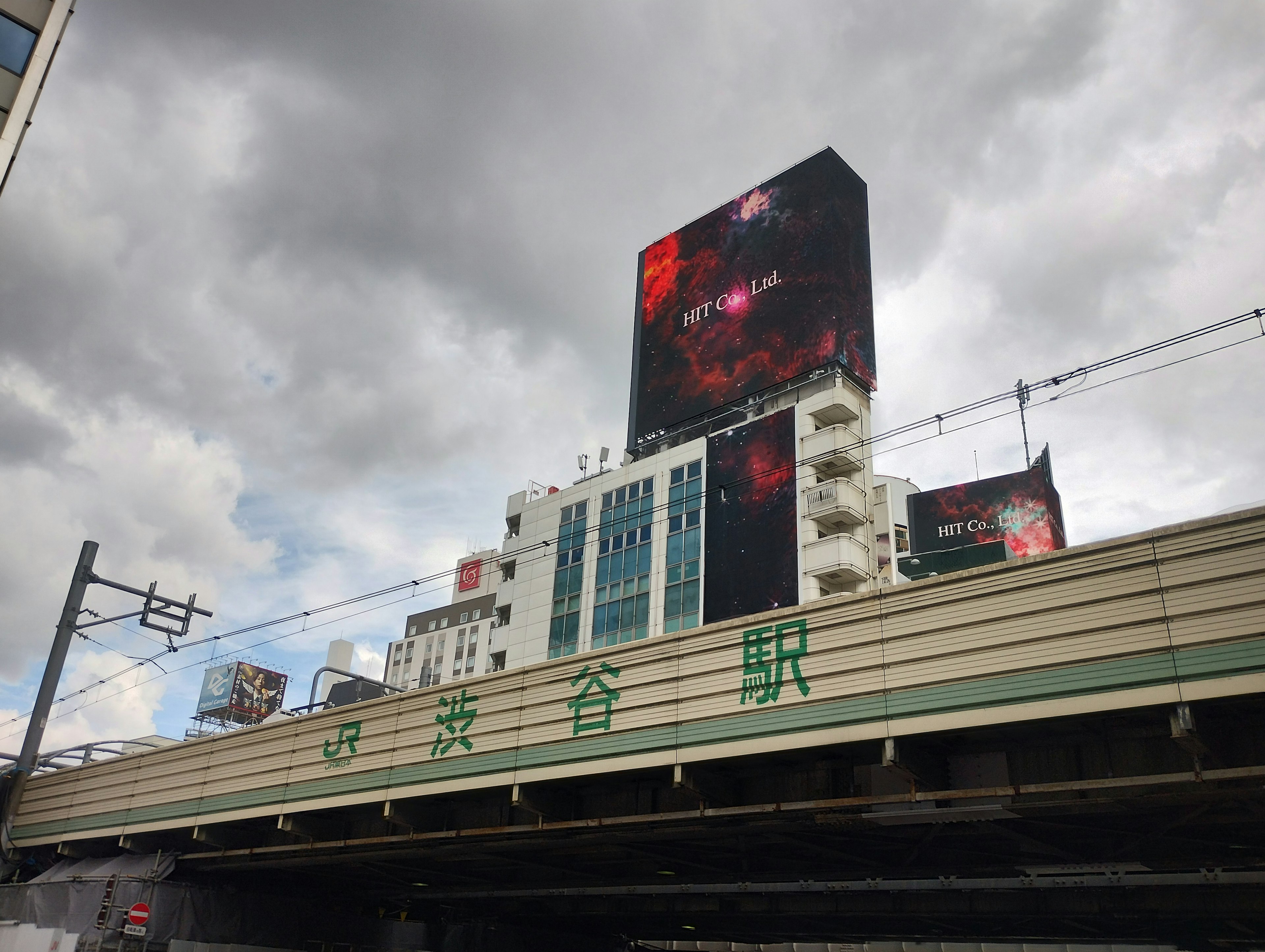 Iklan di atas stasiun kereta dengan langit mendung dan gedung-gedung