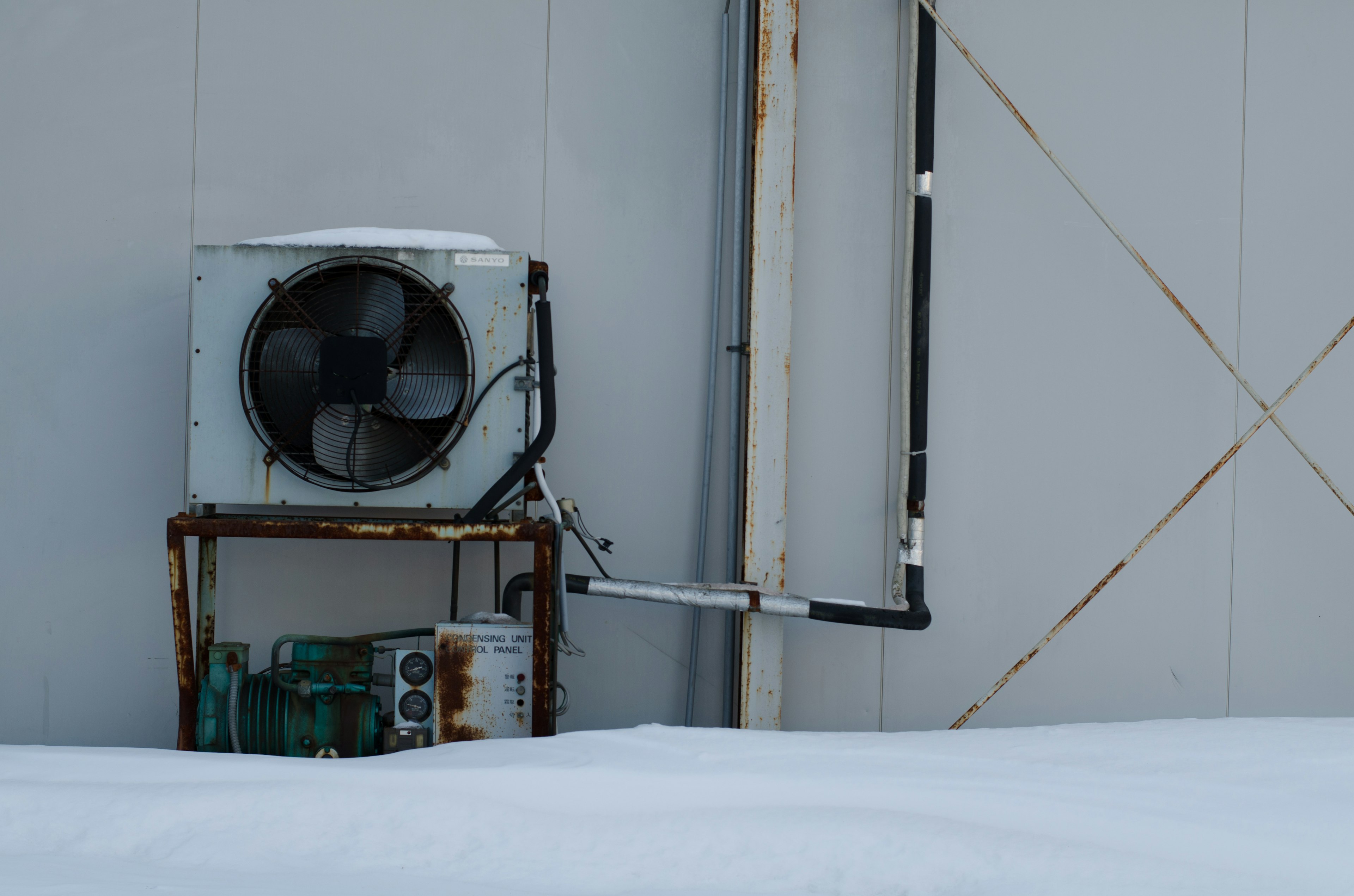 Old air conditioning unit on snow with visible pipes