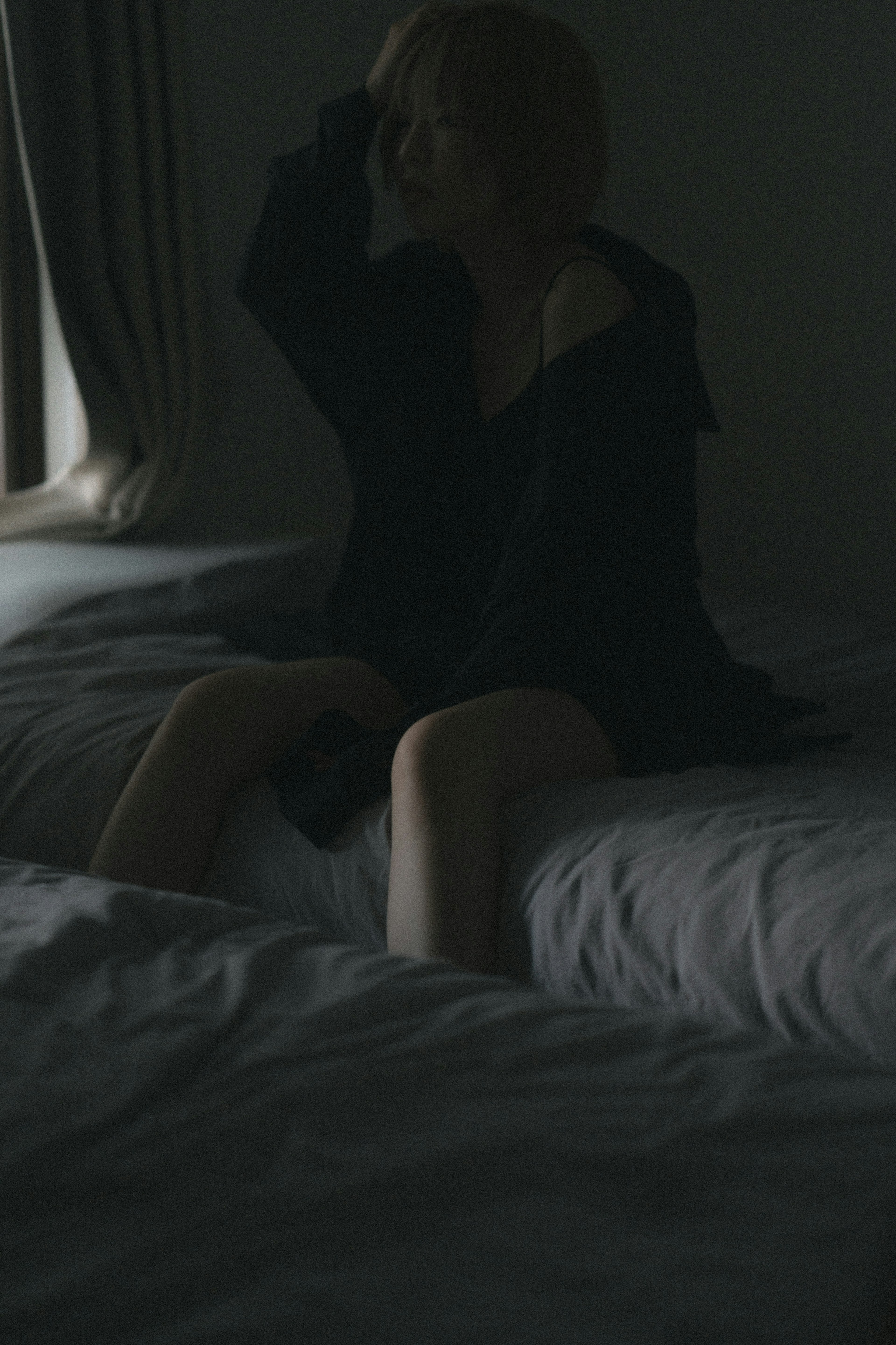 Silhouette of a woman sitting on a bed in a dimly lit room