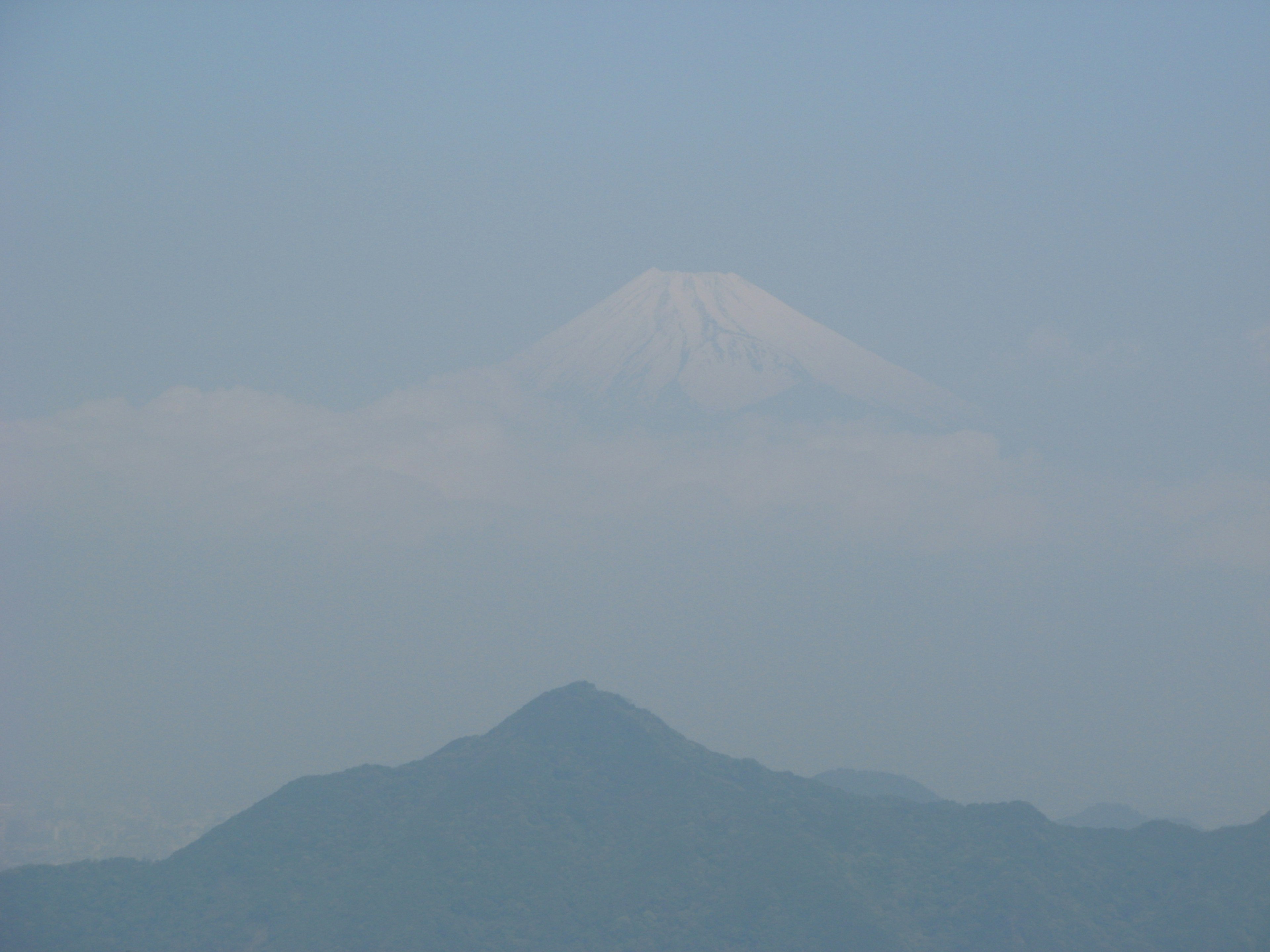 Mount Fuji partially obscured by light clouds under a blue sky