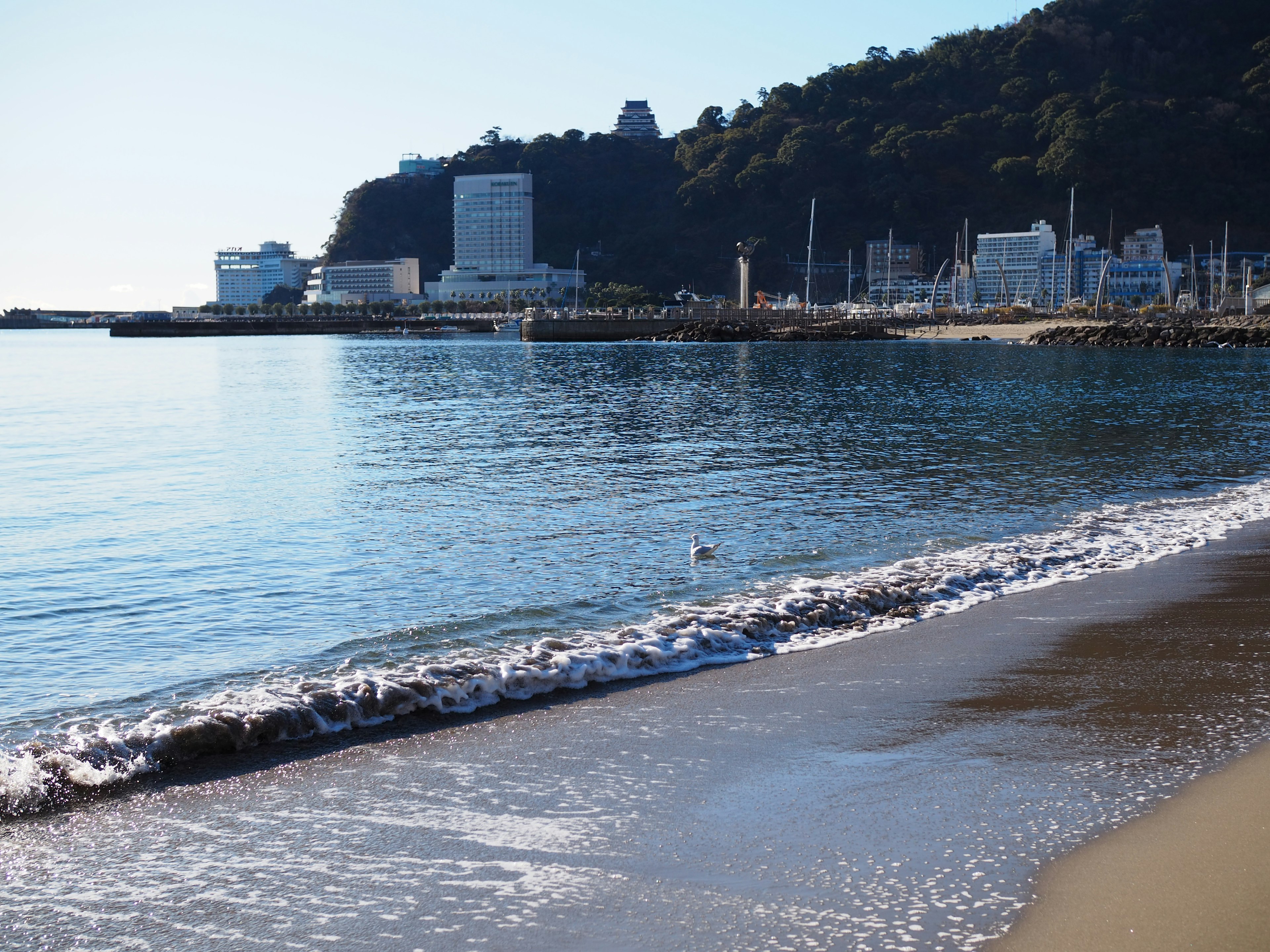 Calm sea and sandy beach scene Harbor buildings and mountain in the background