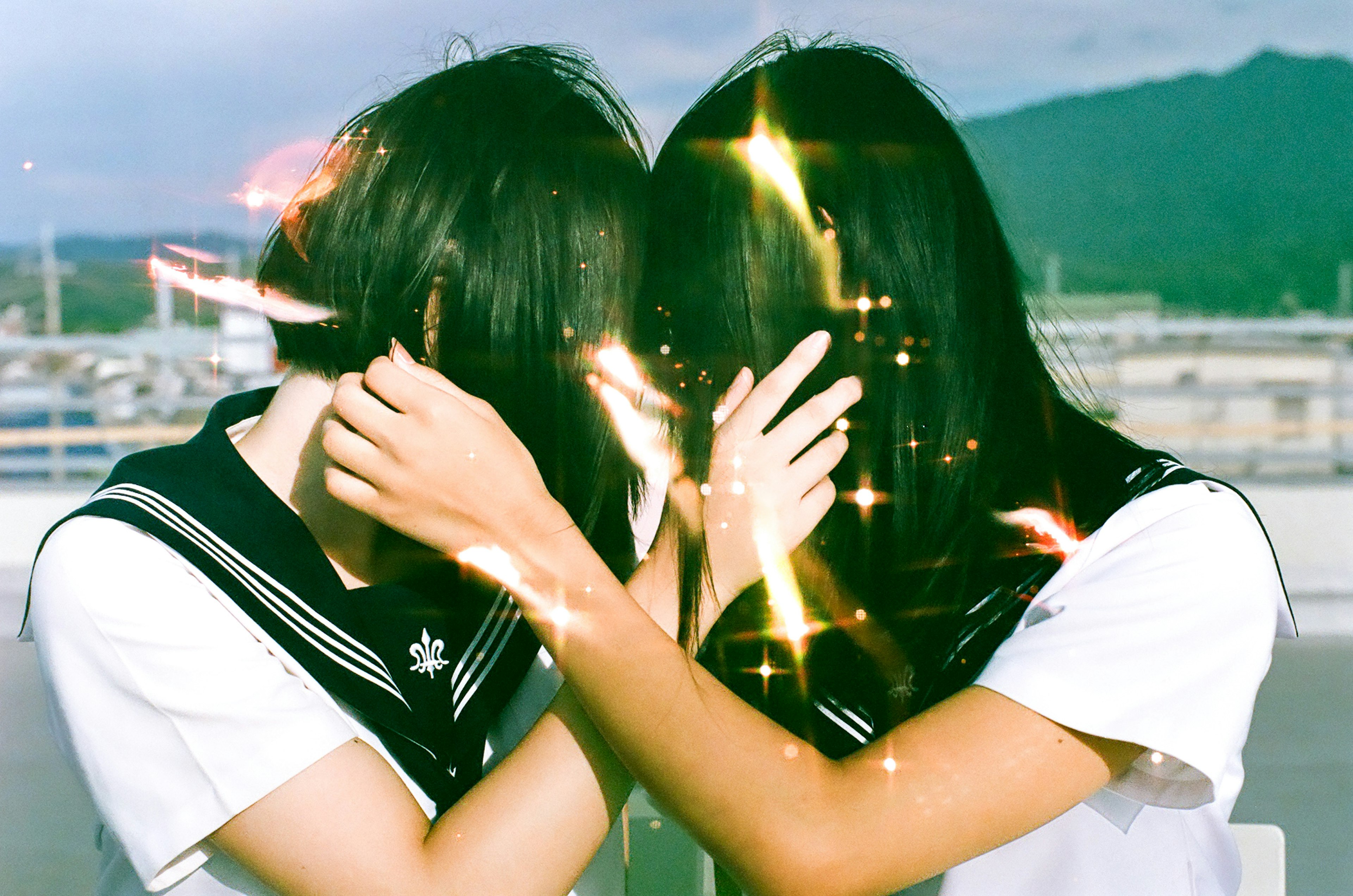 Two students in sailor uniforms closely embracing while hiding their faces with sparkling effects