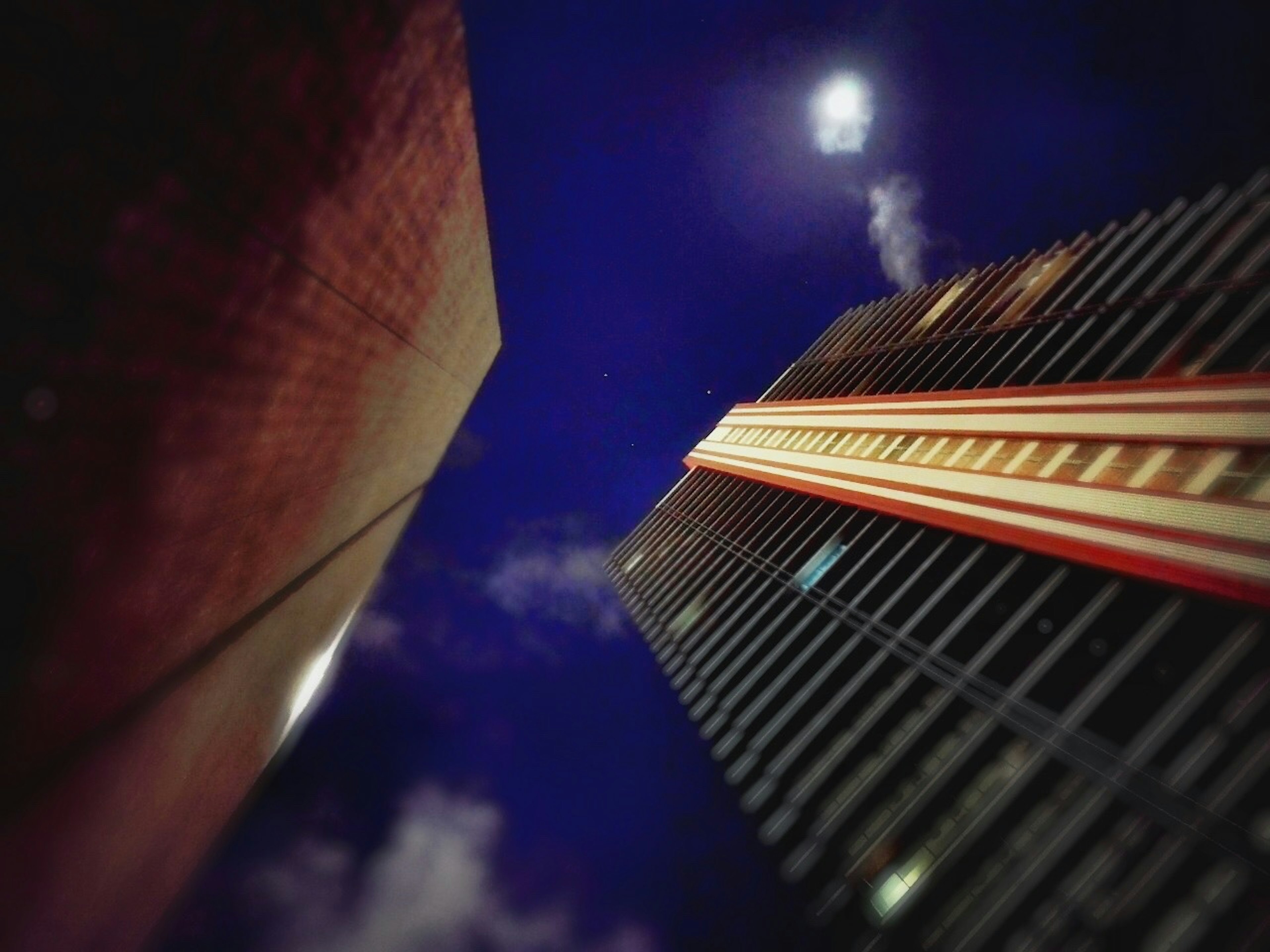 Photo capturing the perspective of skyscrapers under a night sky with a glowing moon