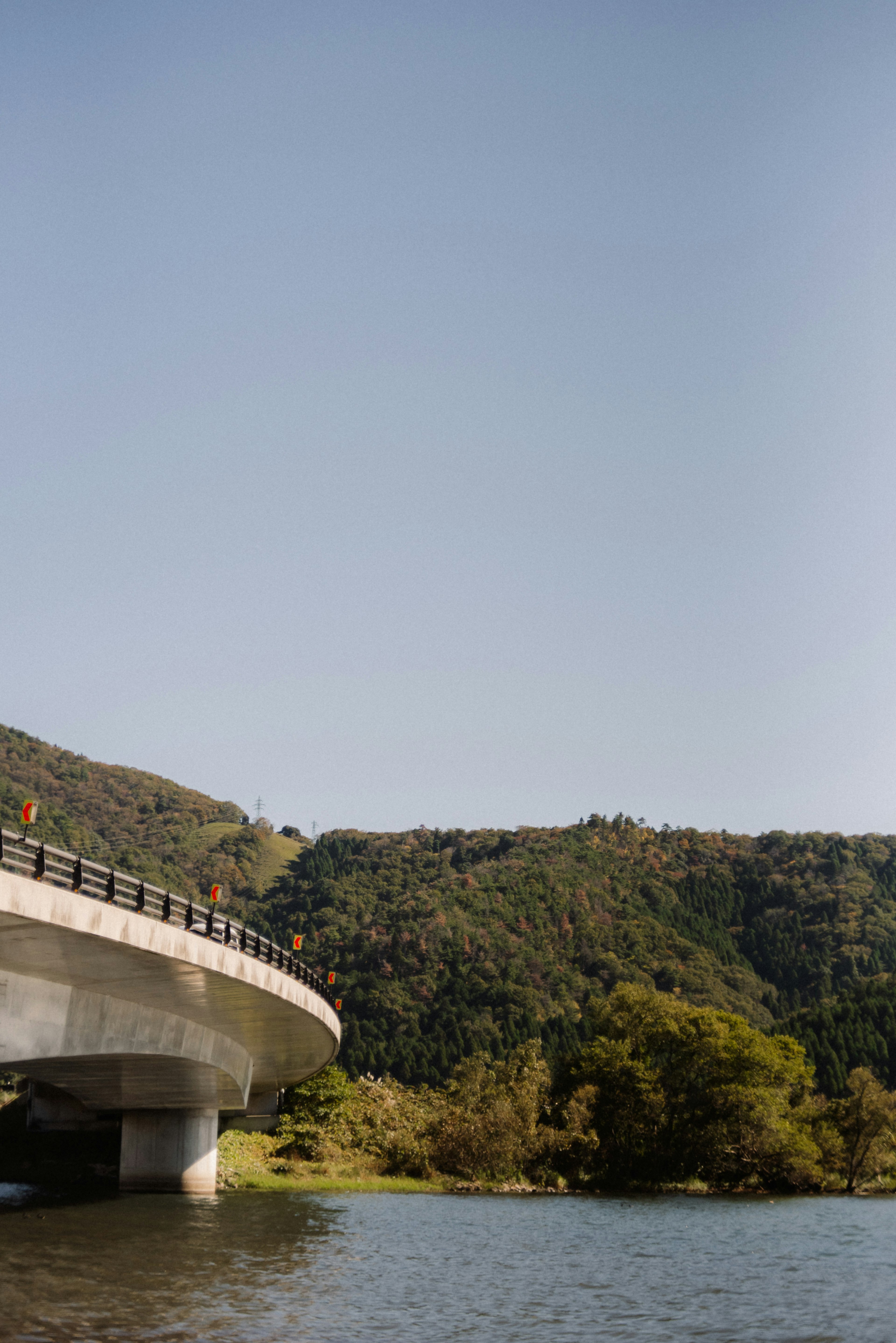 Puente curvado sobre un lago bajo un cielo azul con colinas verdes