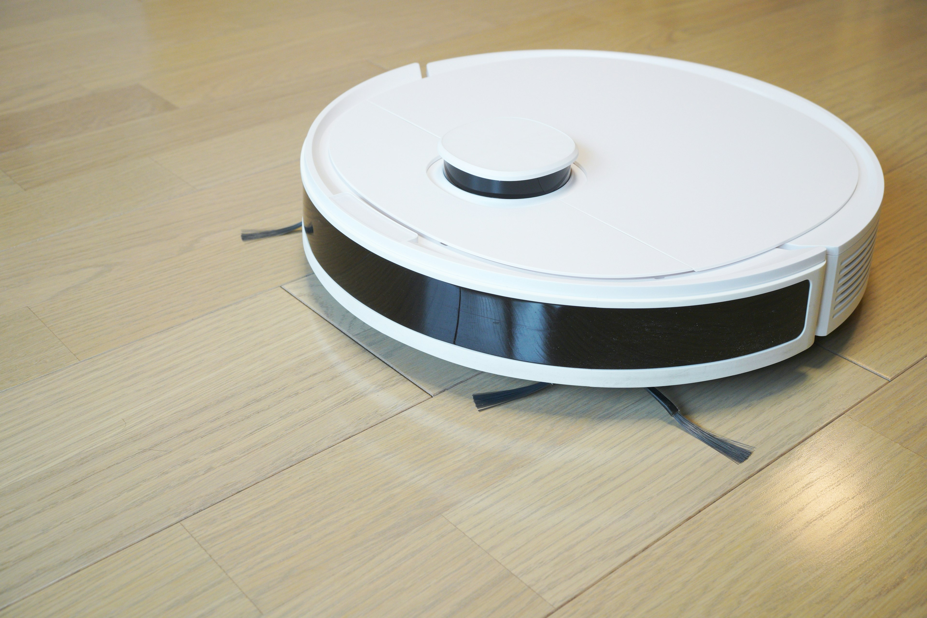 A white robotic vacuum cleaner moving on a wooden floor