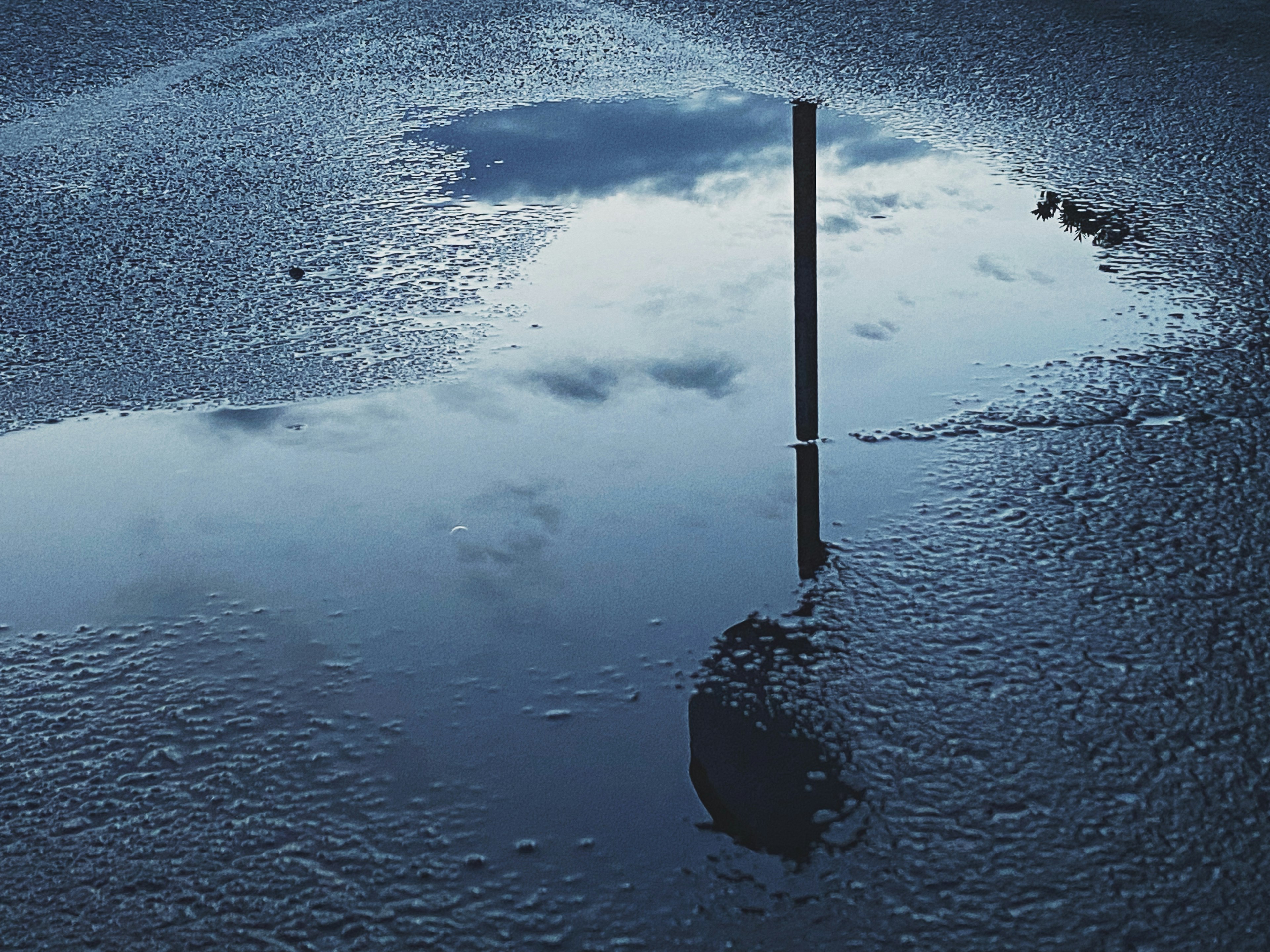 Reflet du ciel et d'un poteau dans une flaque d'eau