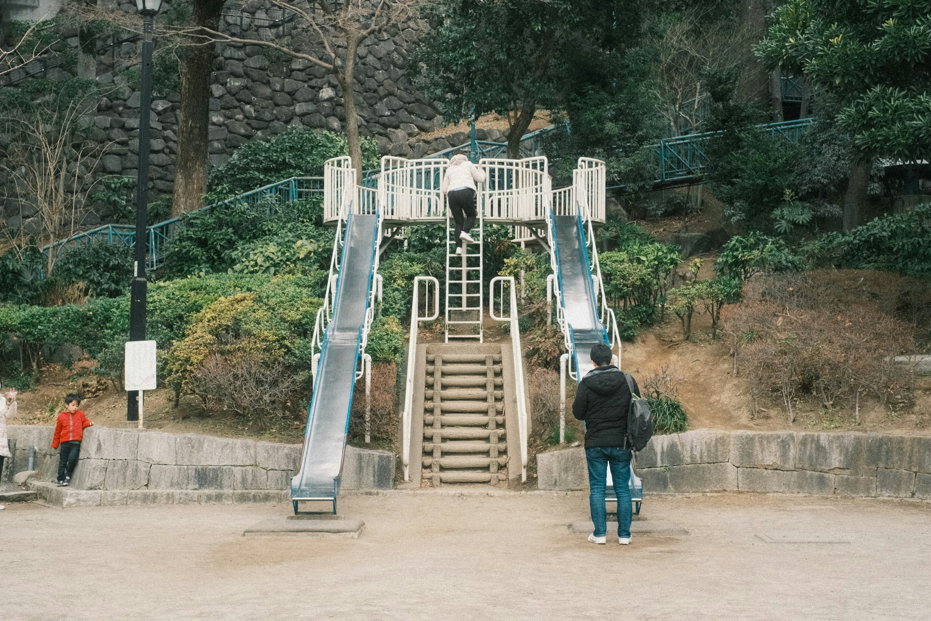 A playground scene featuring slides and stairs with children and adults