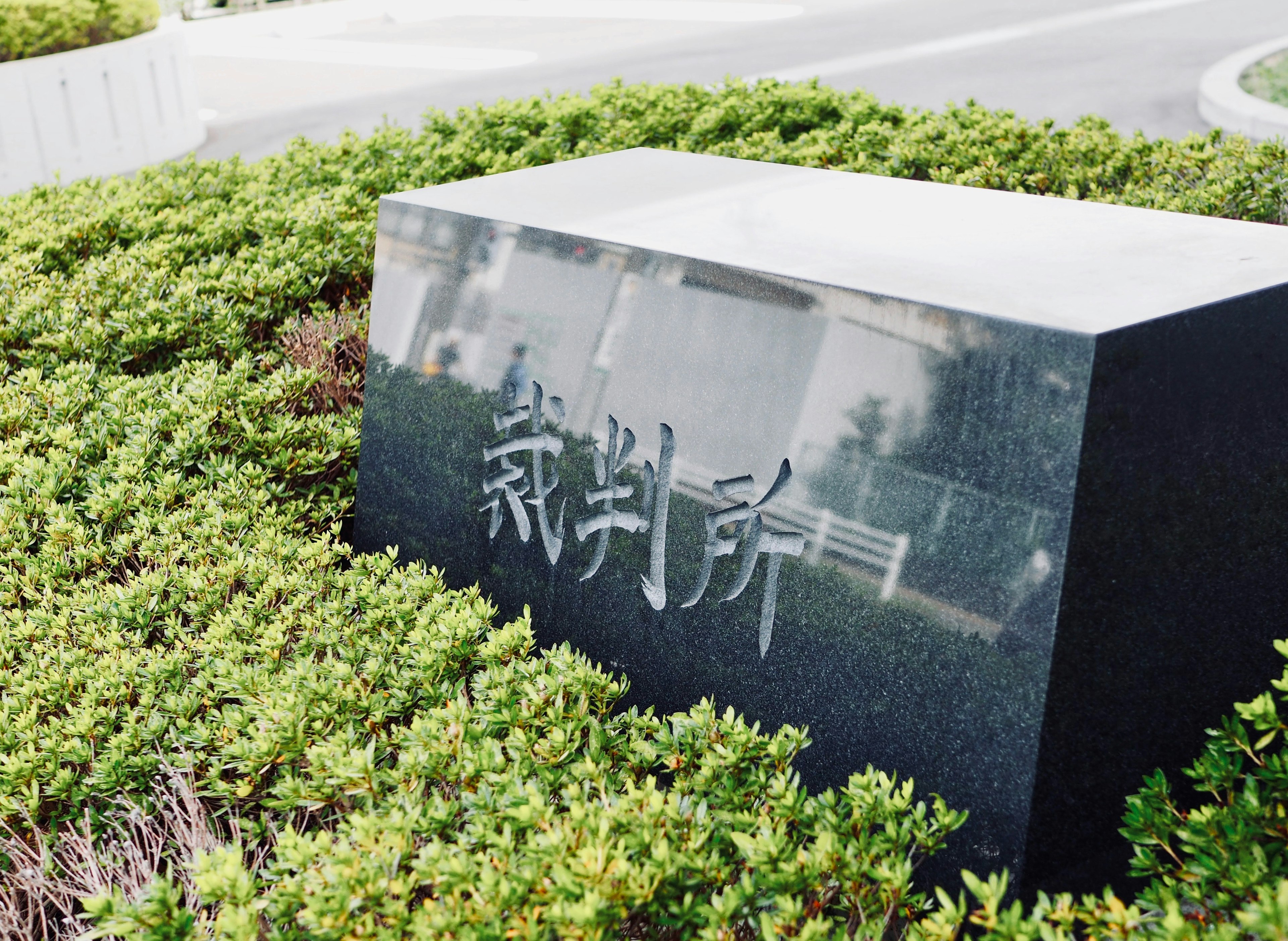 Un monument en pierre noire avec des caractères japonais gravés entouré de buissons verts