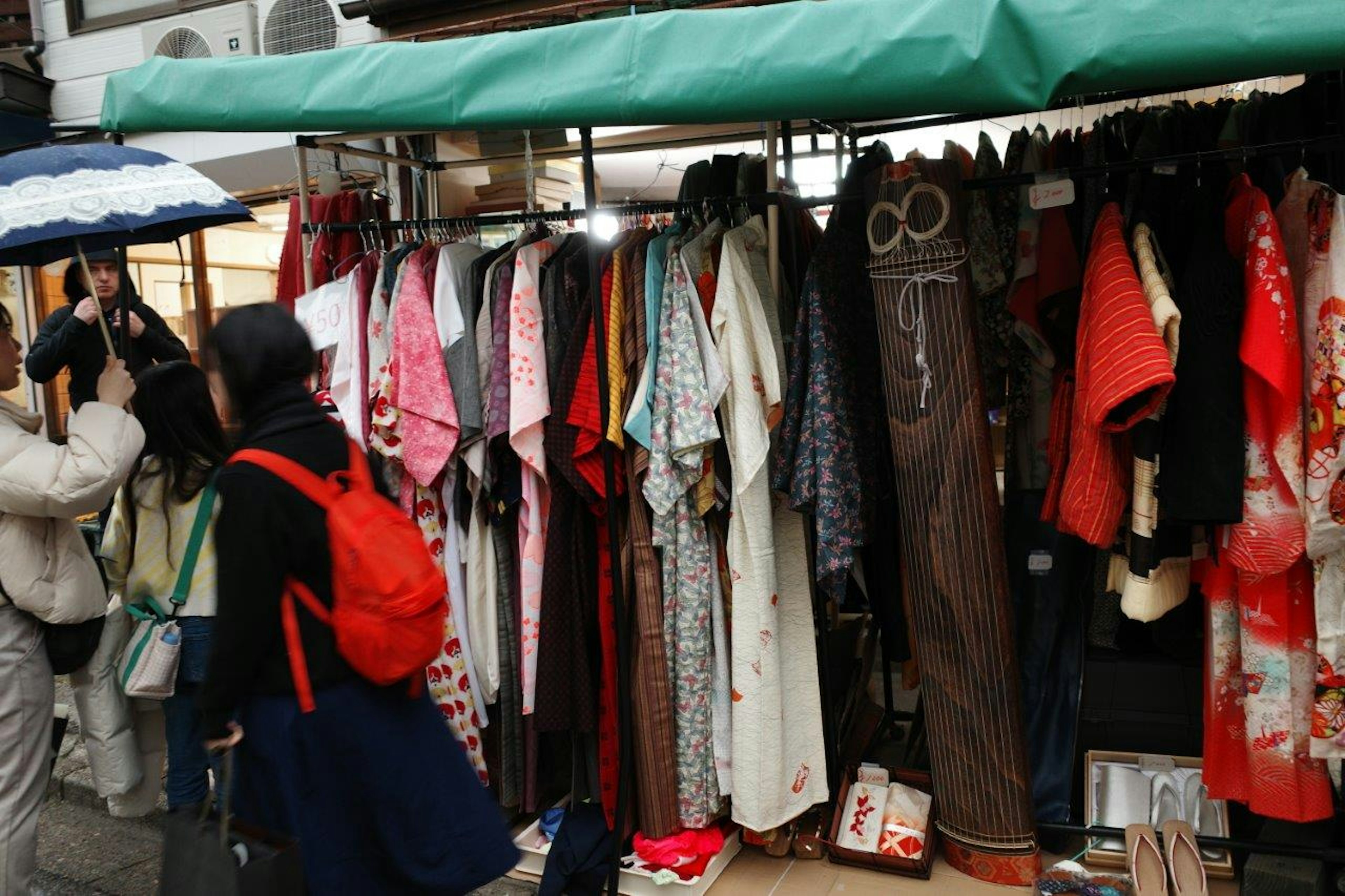 着物が並ぶ屋台と傘を持つ人々の風景