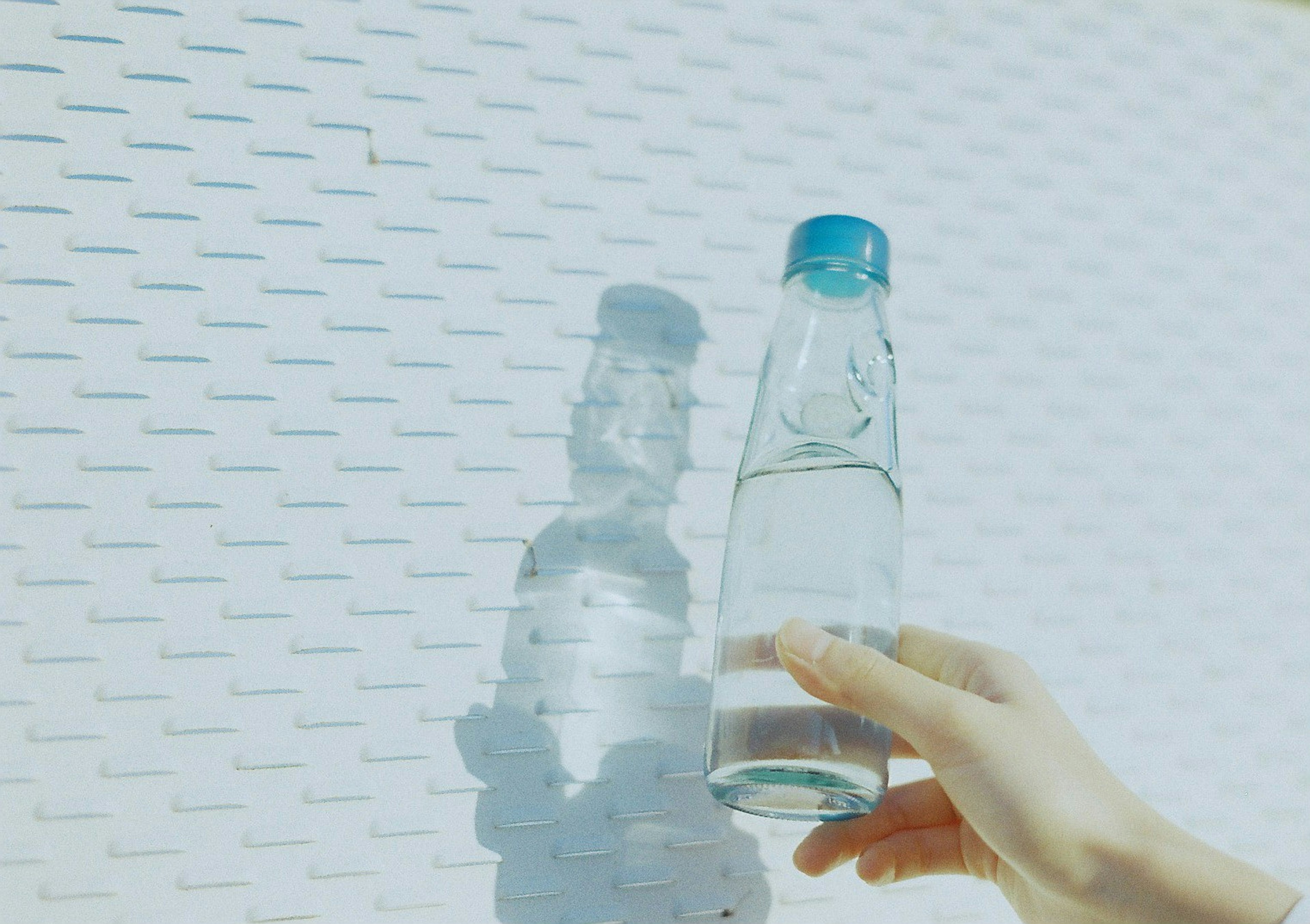 Hand holding a clear water bottle with its shadow on a textured white wall